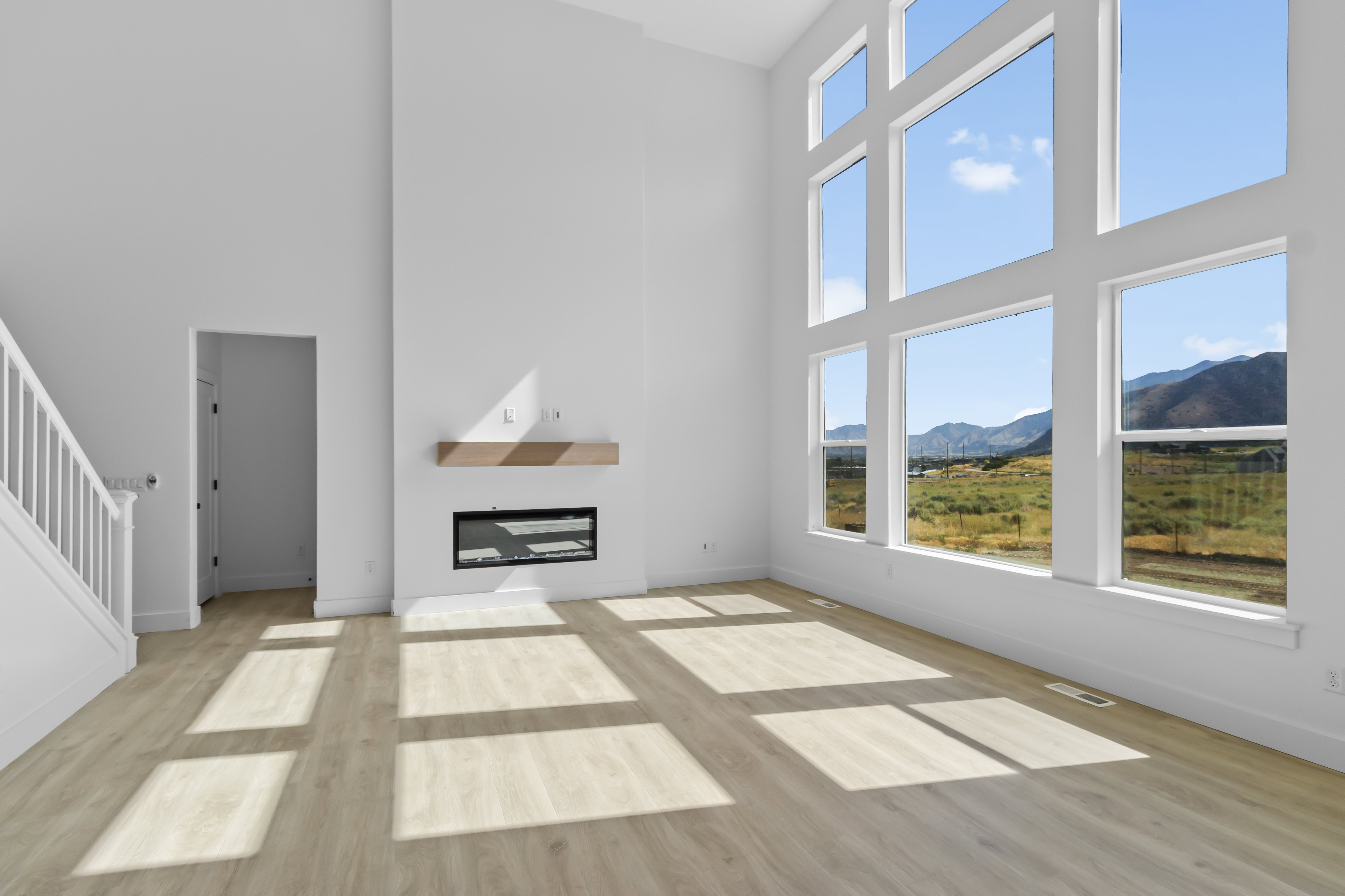 Two-story living area featuring extensive window-walls, a modern linear fireplace with a wood mantel, and light wood-finish flooring