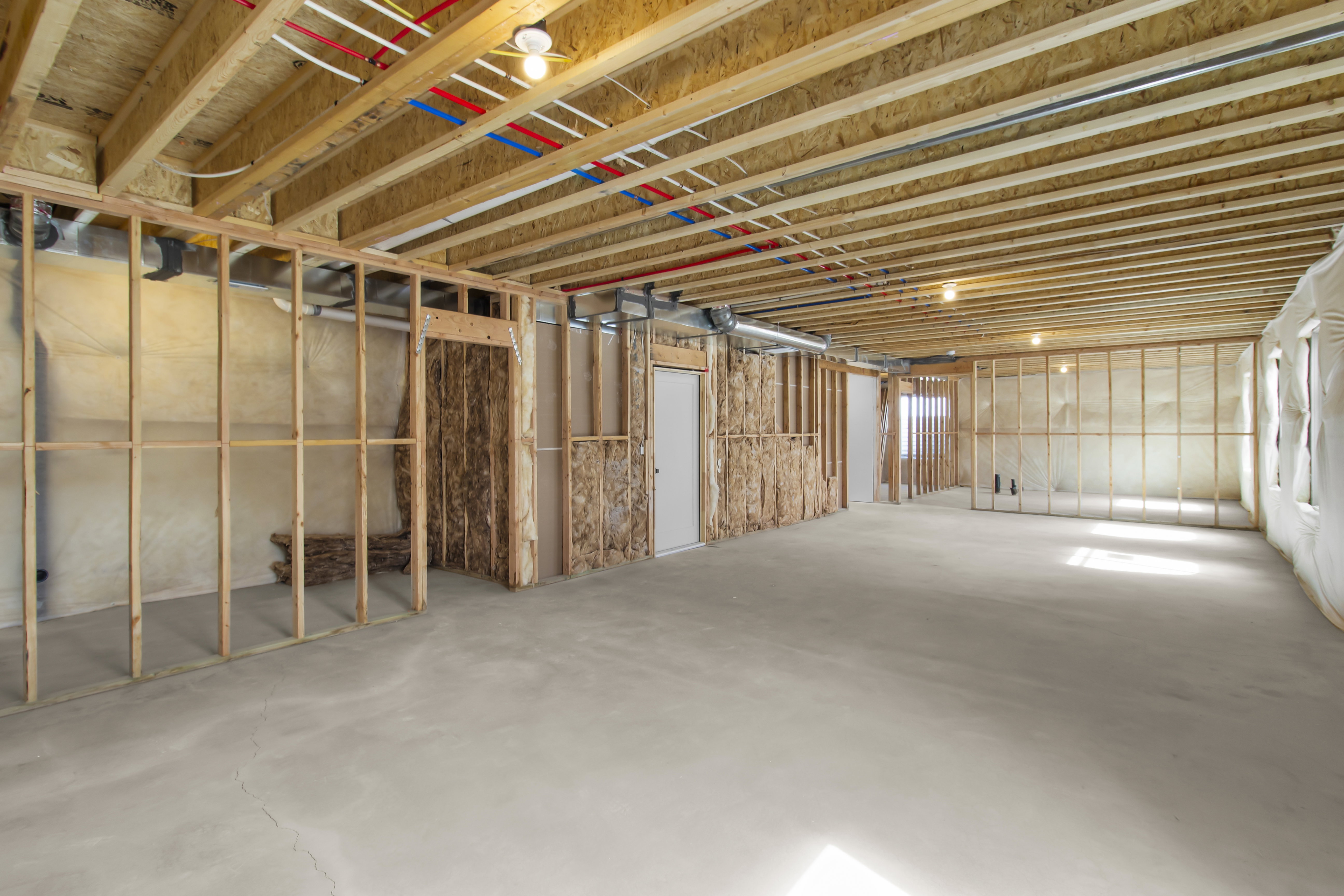 Unfinished lower level featuring concrete flooring, exposed wooden joists, and framed partition walls