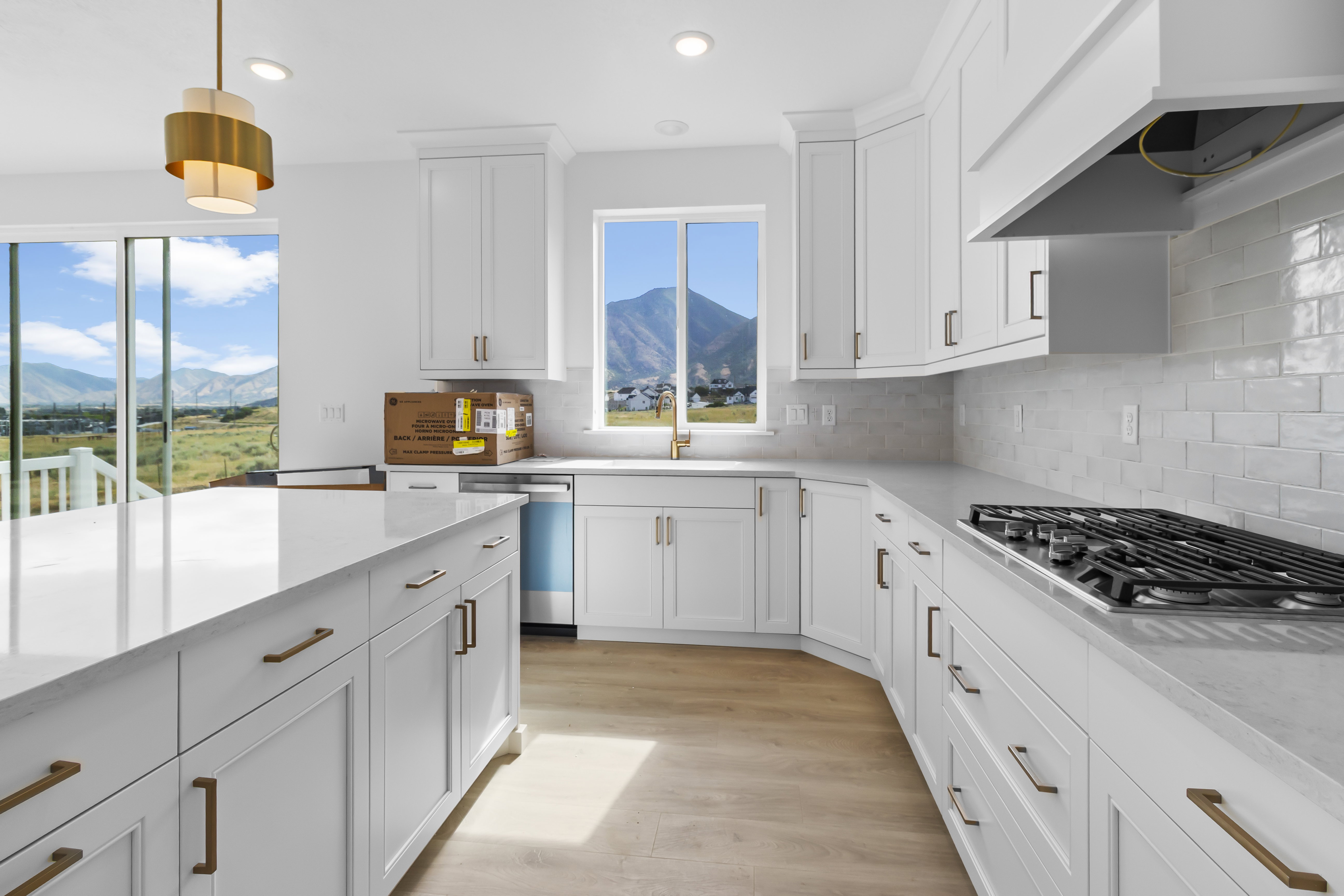 Contemporary kitchen featuring white cabinetry with bronze hardware, a gas range with a matching range hood, and light-colored wood-finish flooring