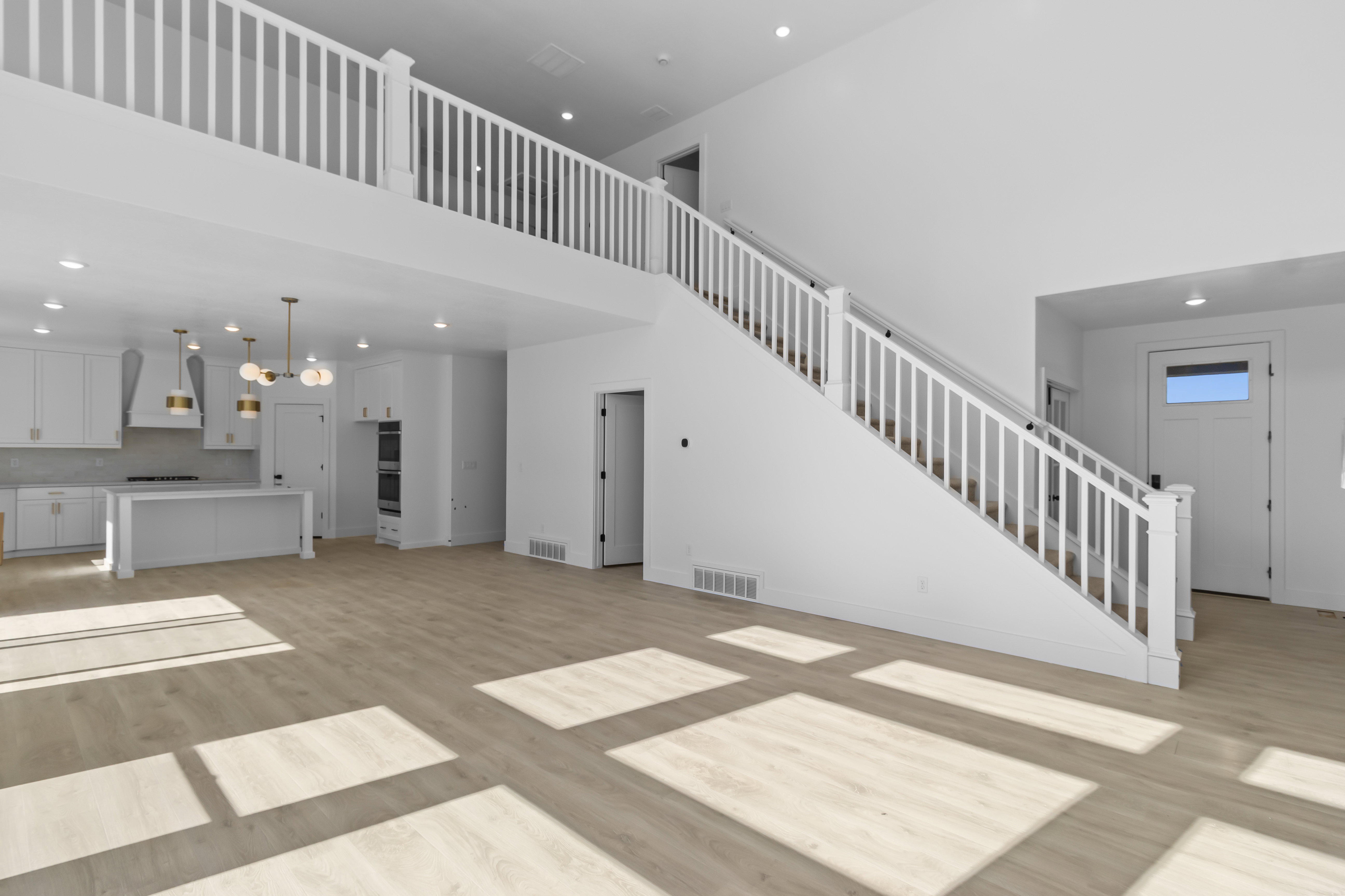 Expansive open-concept living area featuring a two-story ceiling, wood-finish flooring, and a contemporary kitchen