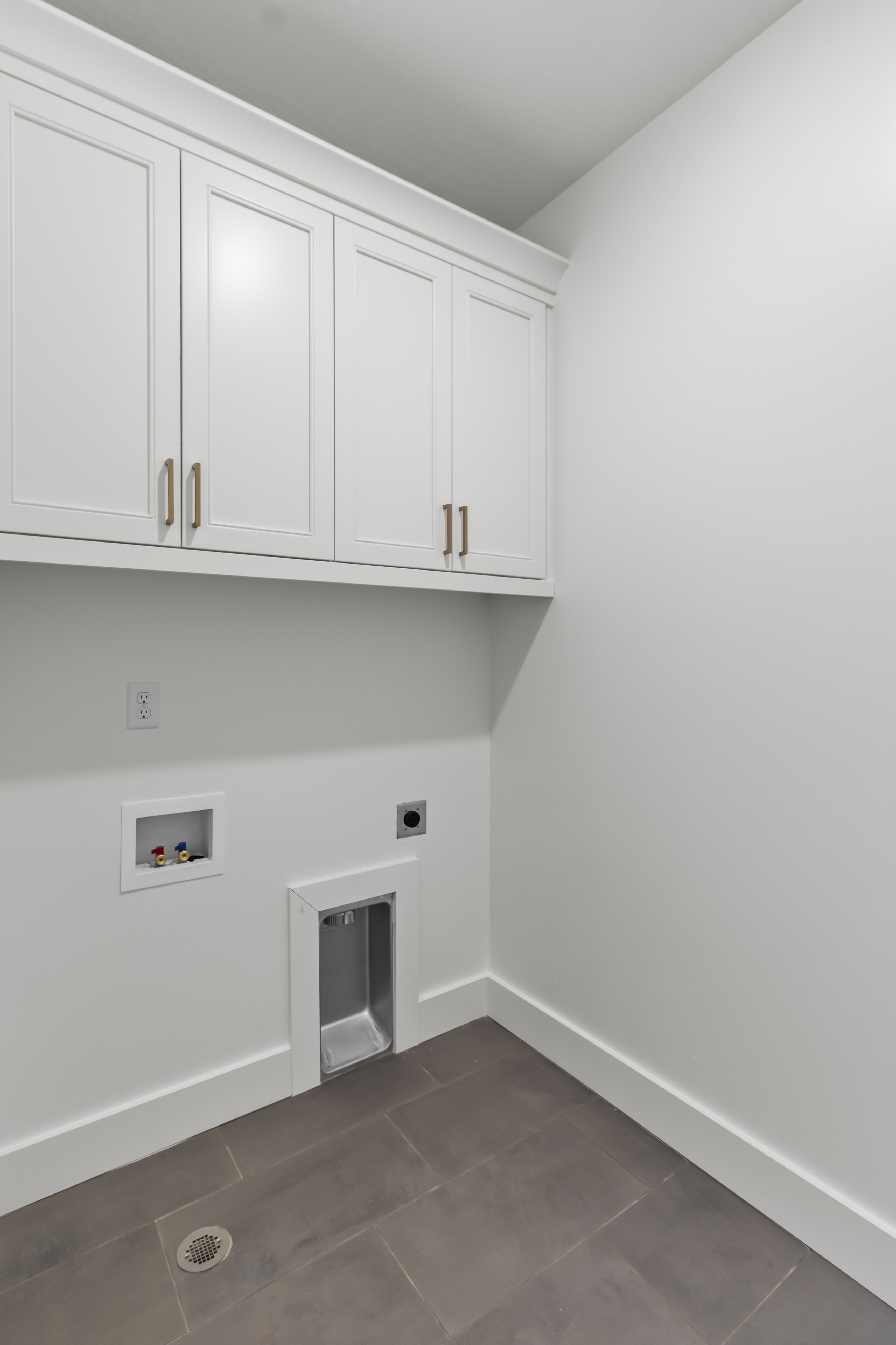 Laundry area featuring overhead white cabinetry with bronze hardware, a floor drain, and gray rectangular floor tiles