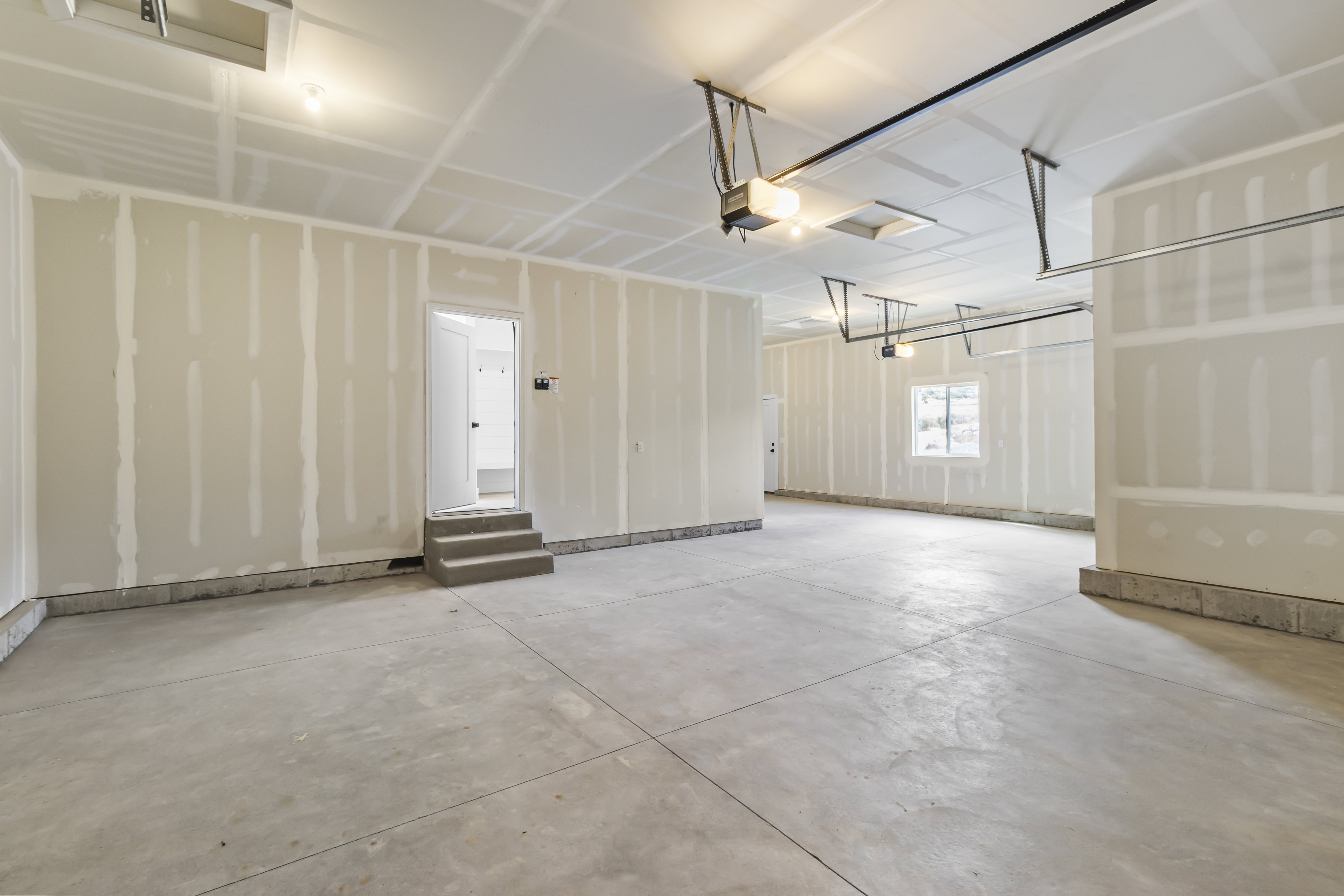 Spacious unfinished garage featuring concrete flooring, unpainted drywall, and exposed ceiling framing