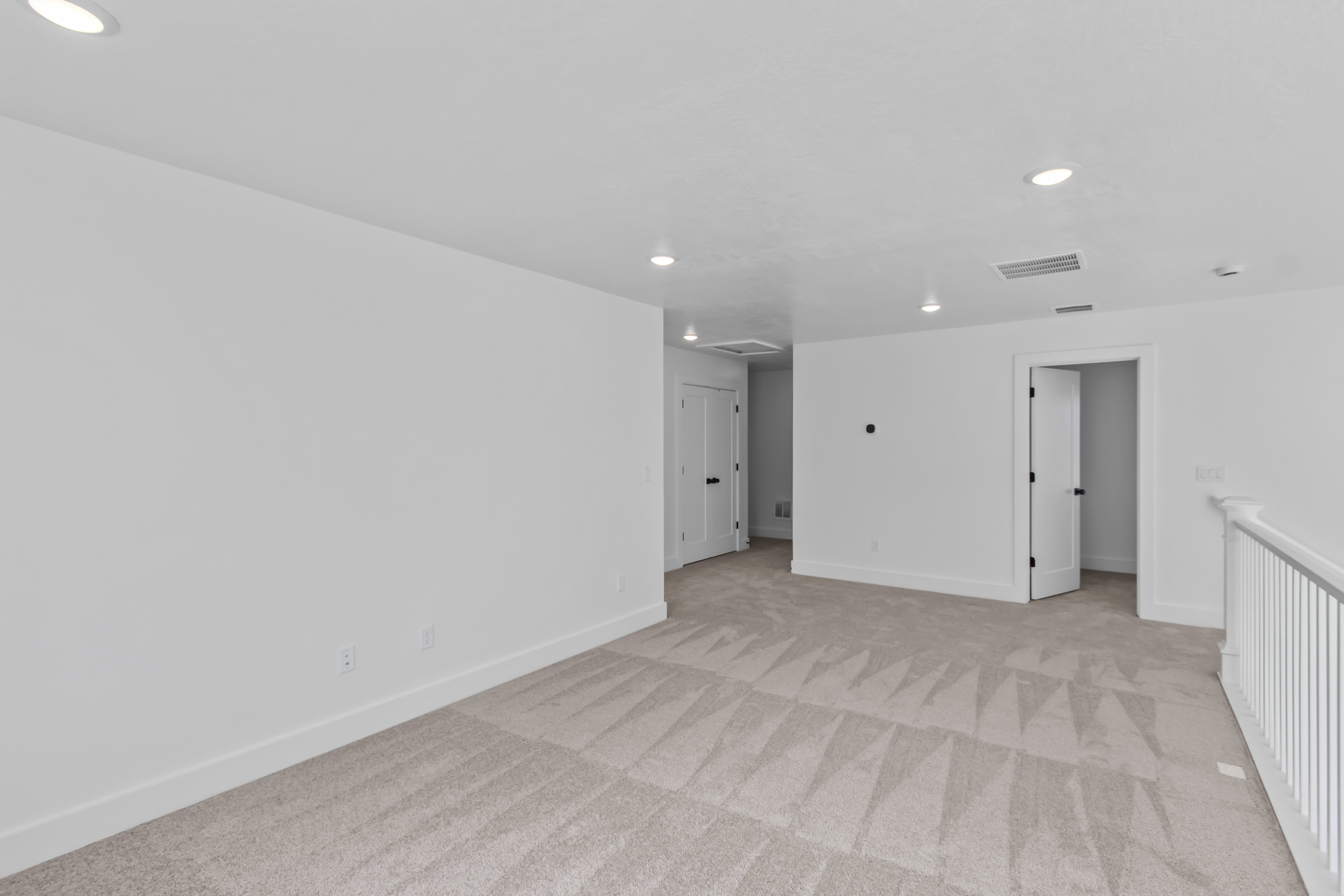 Spacious carpeted room featuring white walls, white trim, recessed lighting, and multiple doorways