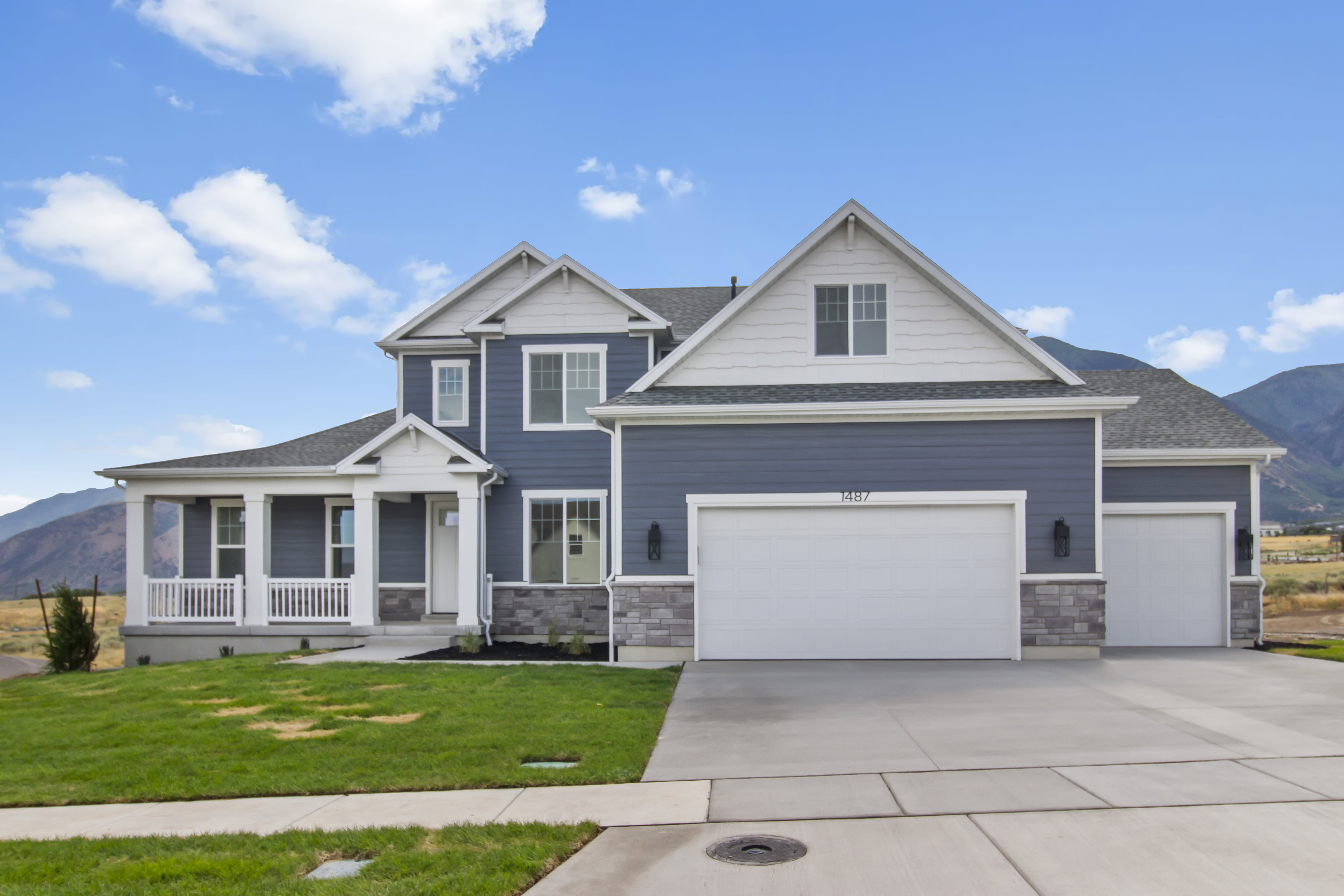 Contemporary residence featuring a blue siding exterior with white trim, a covered front porch, an attached multi-car garage, and a concrete driveway