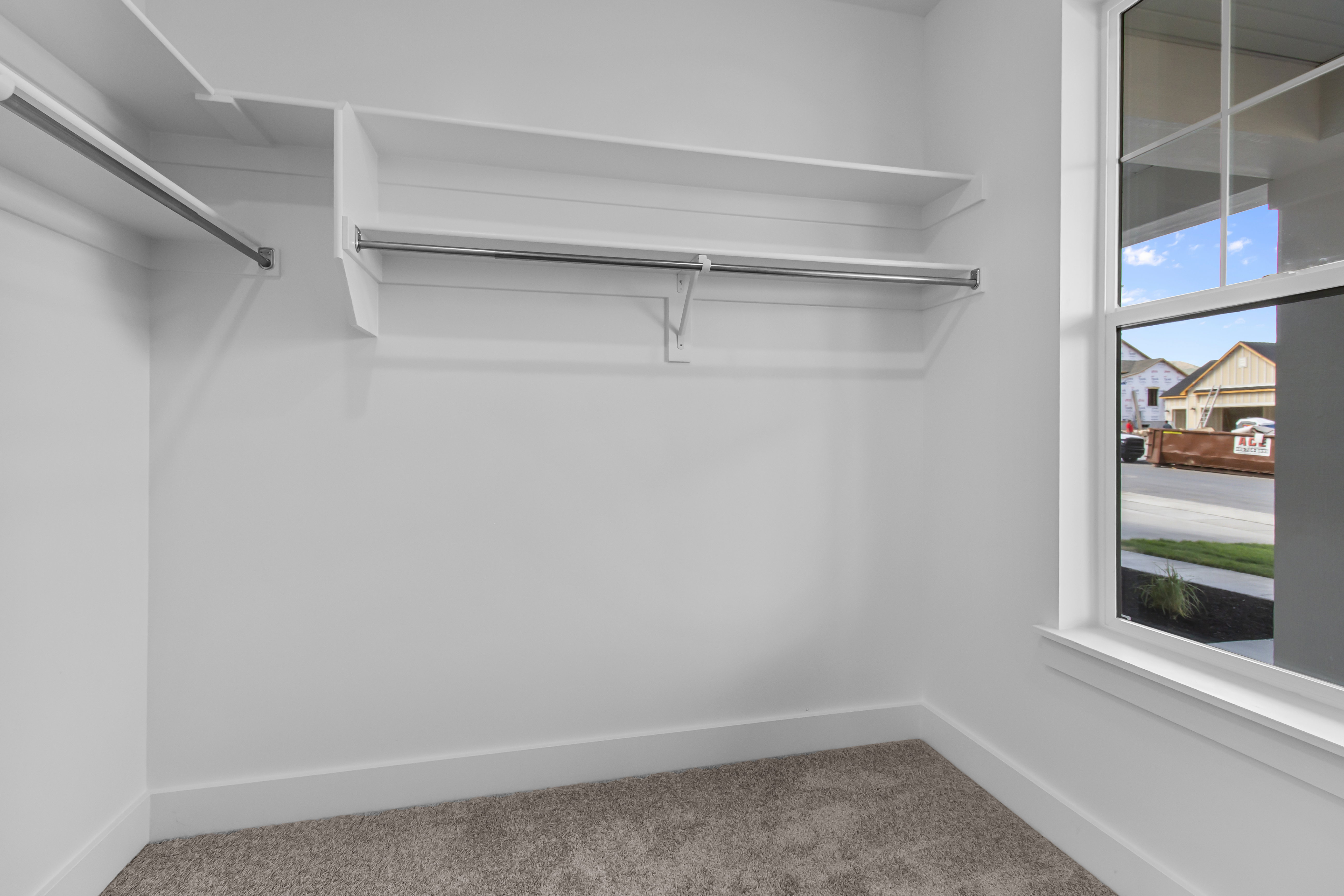 Spacious closet featuring built-in shelving, two hanging rods, plush carpet flooring, a large window, and white trim
