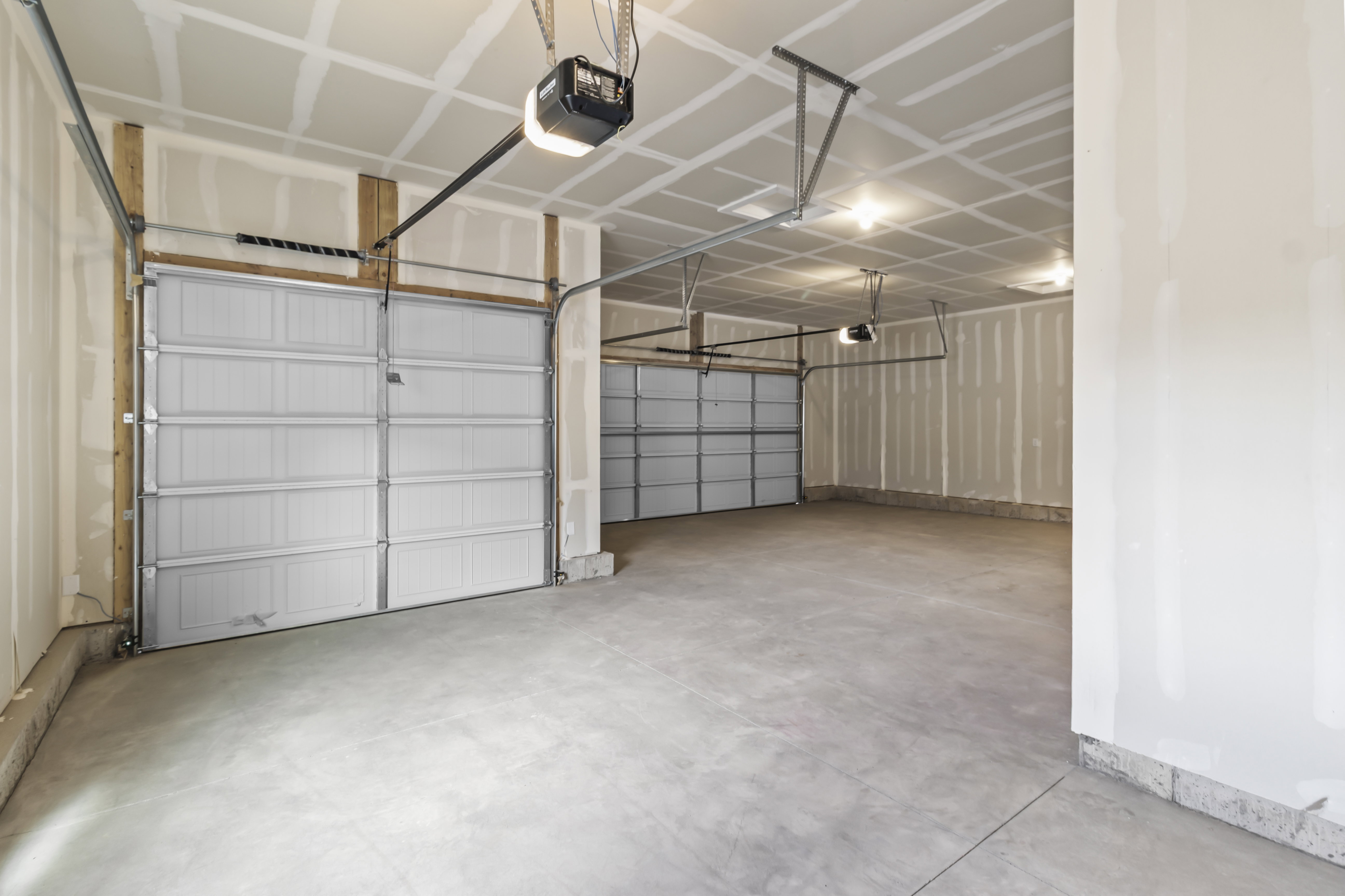 Spacious multi-car garage featuring a concrete floor, two white paneled garage doors, and overhead lighting