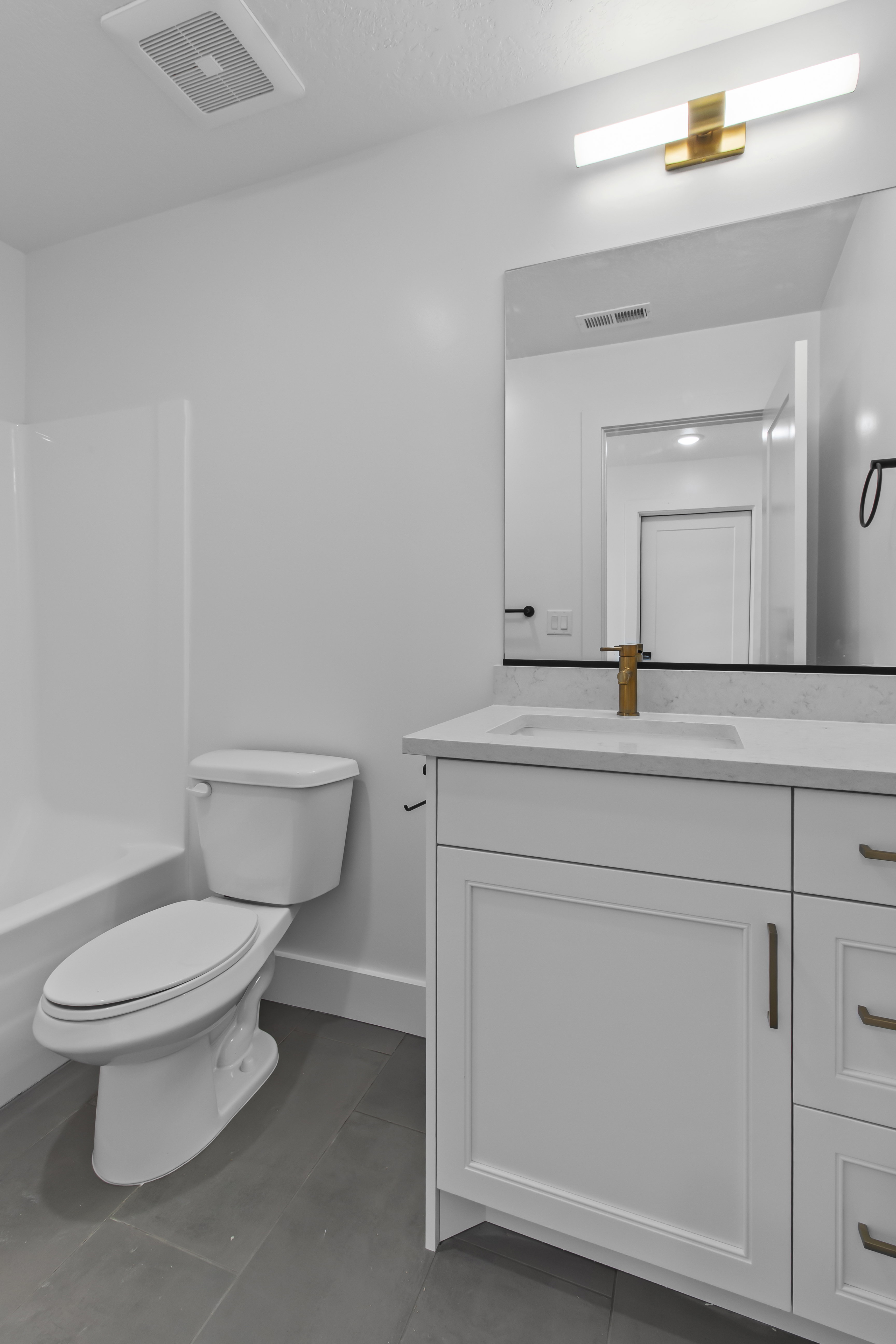 Modern bathroom featuring a white vanity with shaker-style cabinetry, a built-in sink, and a gold-tone faucet