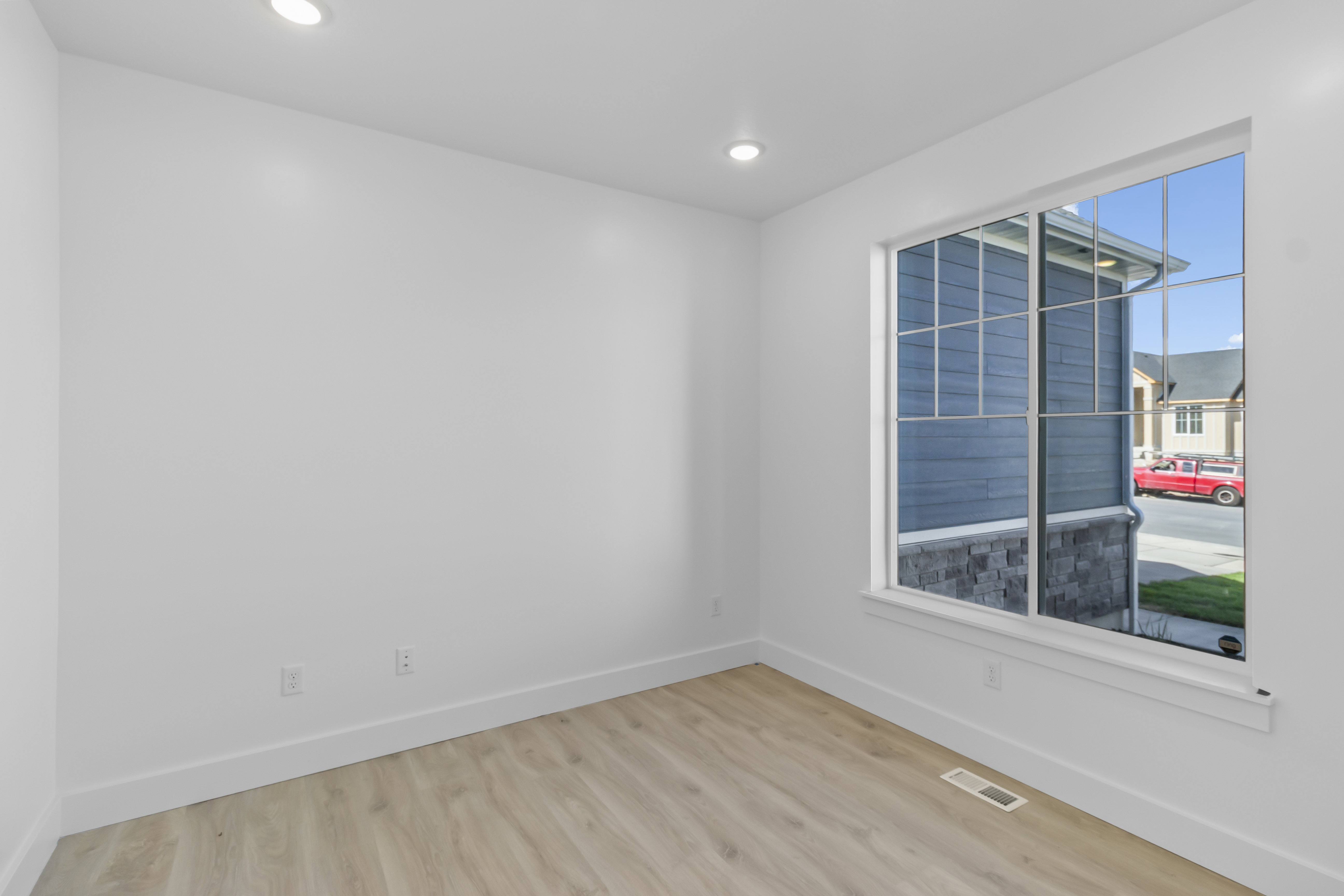 Bright room featuring a large window with grid pattern, recessed lighting, light wood-finish flooring, and white baseboards