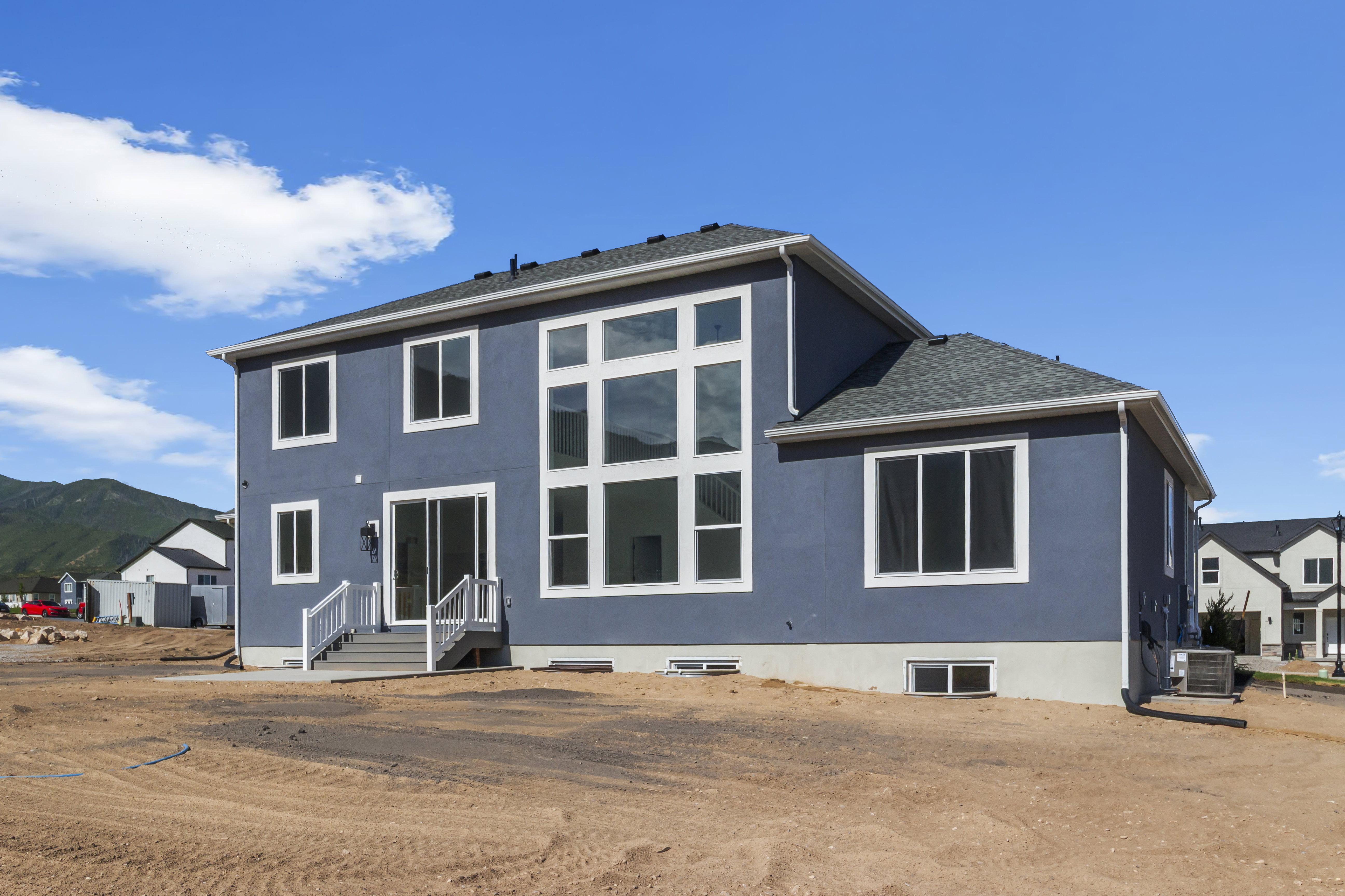 Rear exterior featuring a large window wall, sliding glass door with exterior lighting, and a grey staircase with white railings