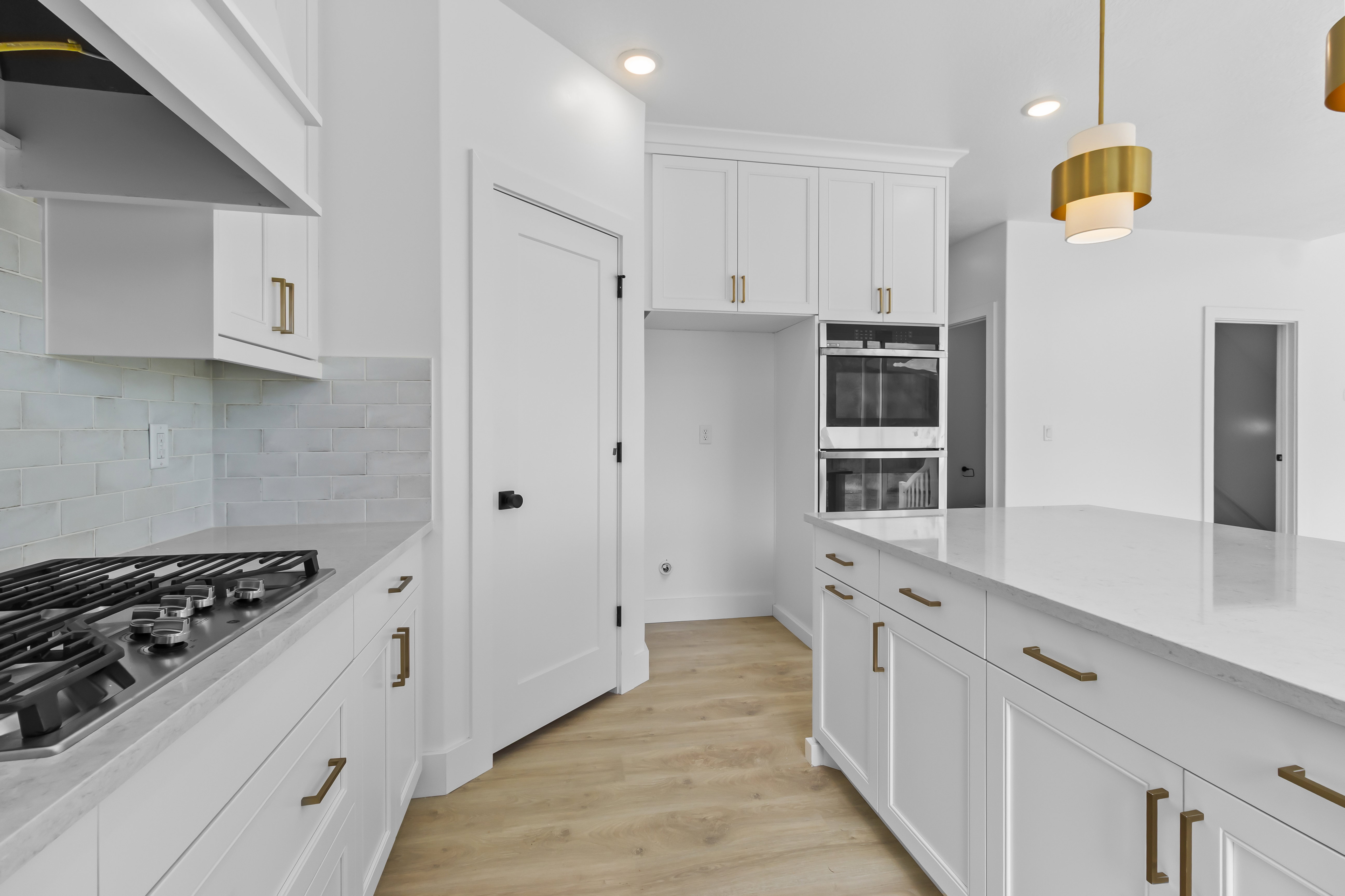 Gourmet kitchen featuring a gas range, white shaker cabinetry, light-toned backsplash, built-in double ovens, and a spacious island with a light-colored countertop
