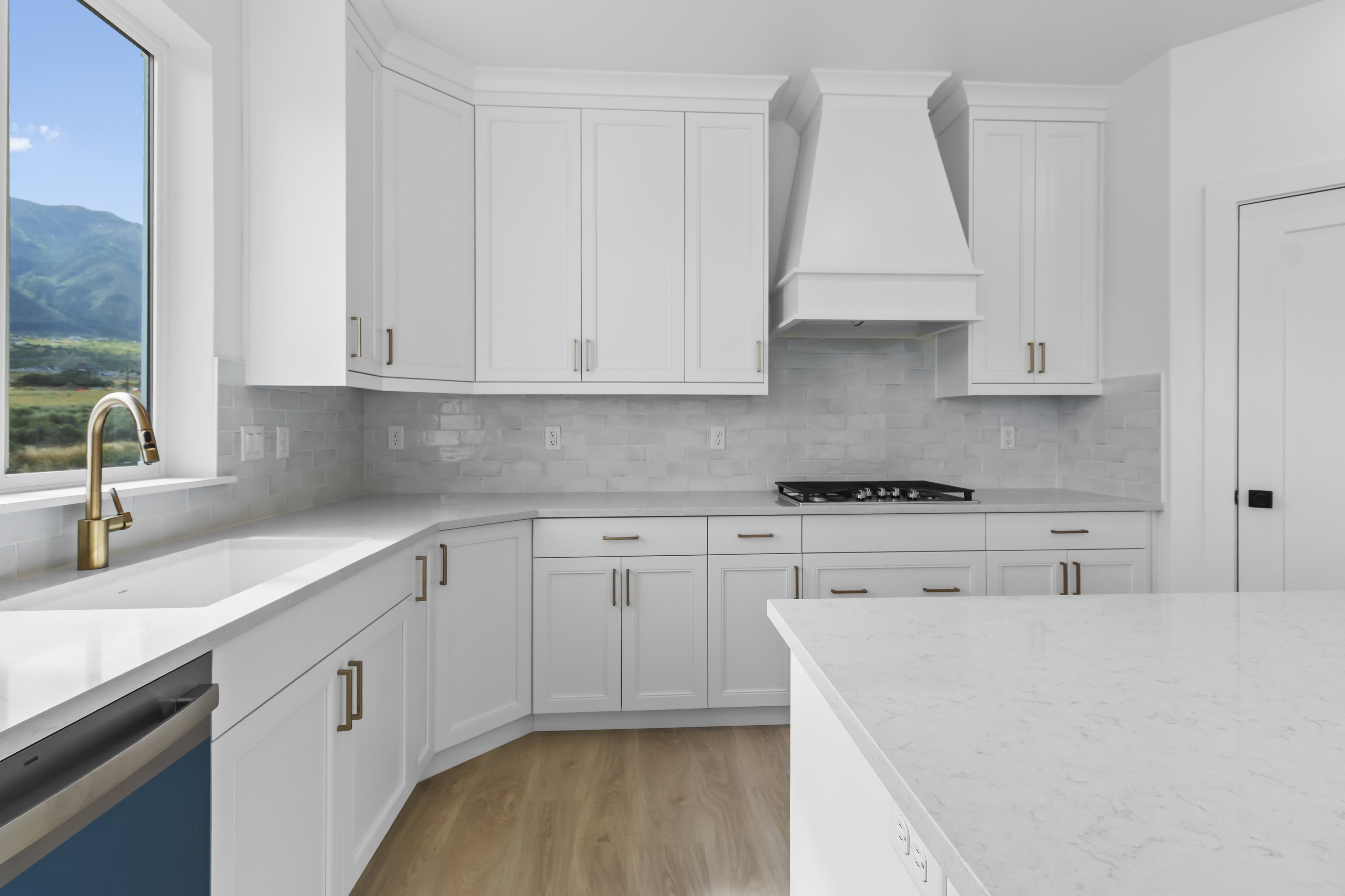Modern kitchen featuring white shaker cabinetry, light-toned countertops, a full tile backsplash, a gas cooktop, and brass hardware
