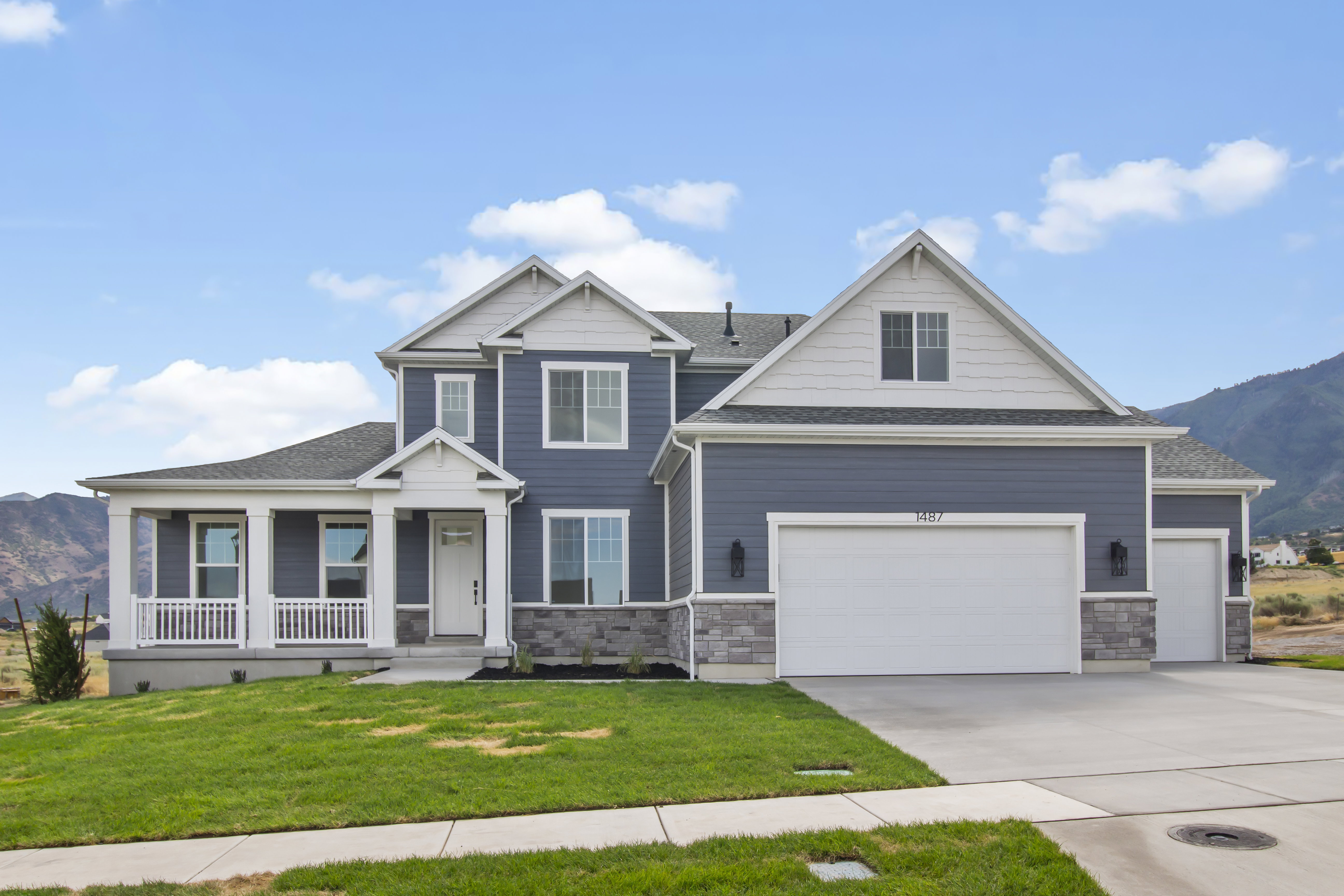 Modern Colonial-style residence featuring a blue siding exterior, white trim accents, a covered front porch with railing, a two-car garage, and an additional single-car garage