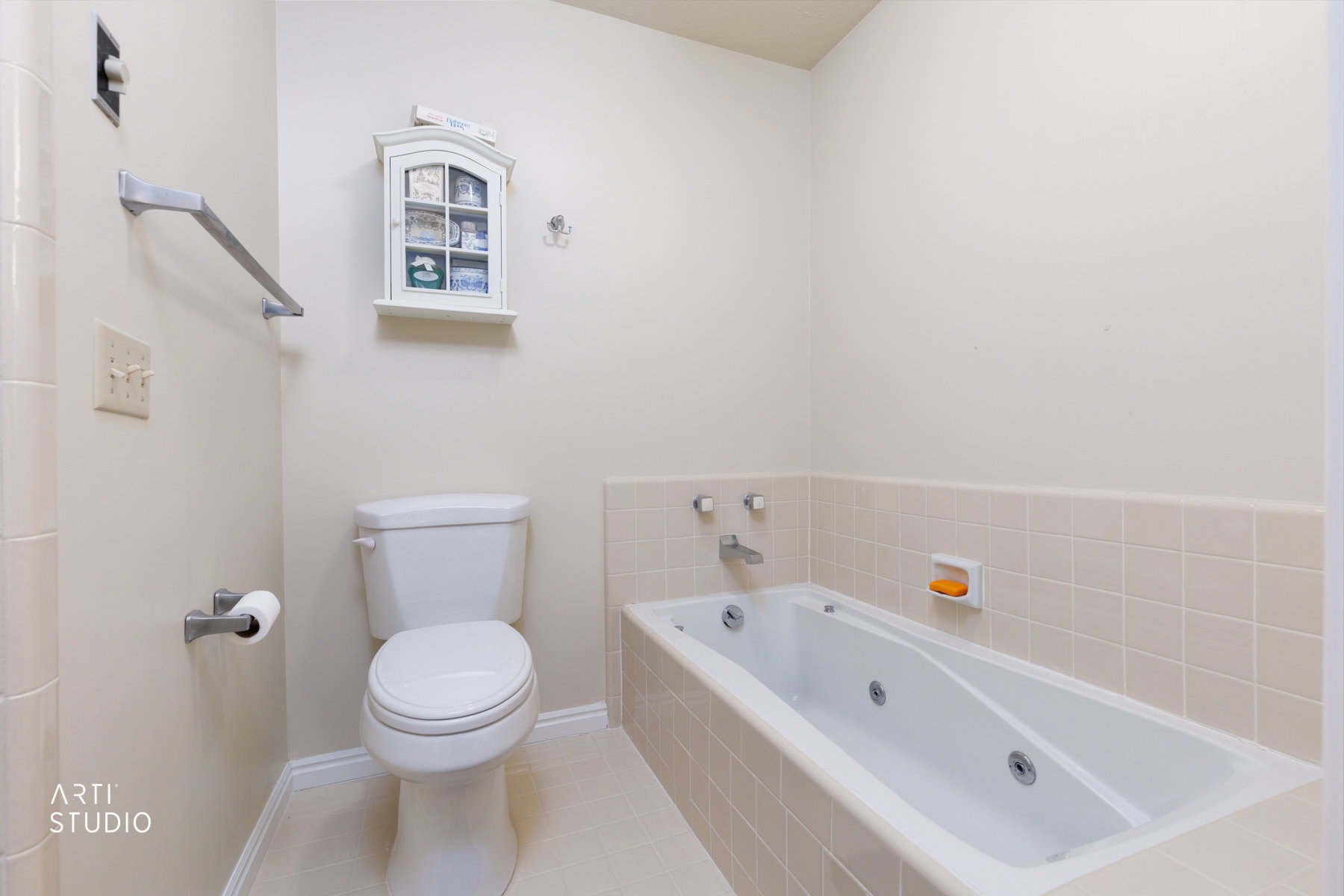 Master bathroom featuring a white toilet, jetted bathtub, tiled surround, and neutral wall tones
