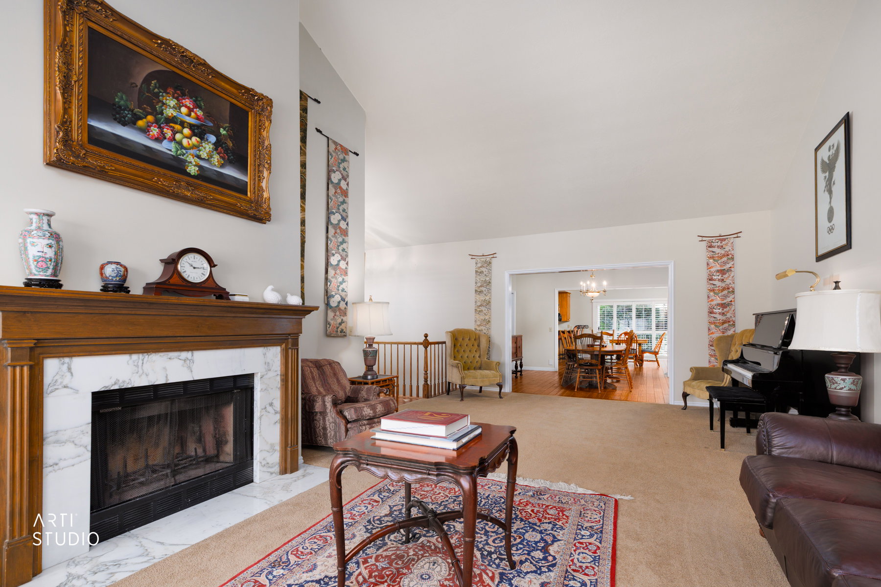 Spacious living area featuring a fireplace with a wood mantel and marble-finish surround, carpet flooring, and a broad entry to a dining space with wood-finish flooring