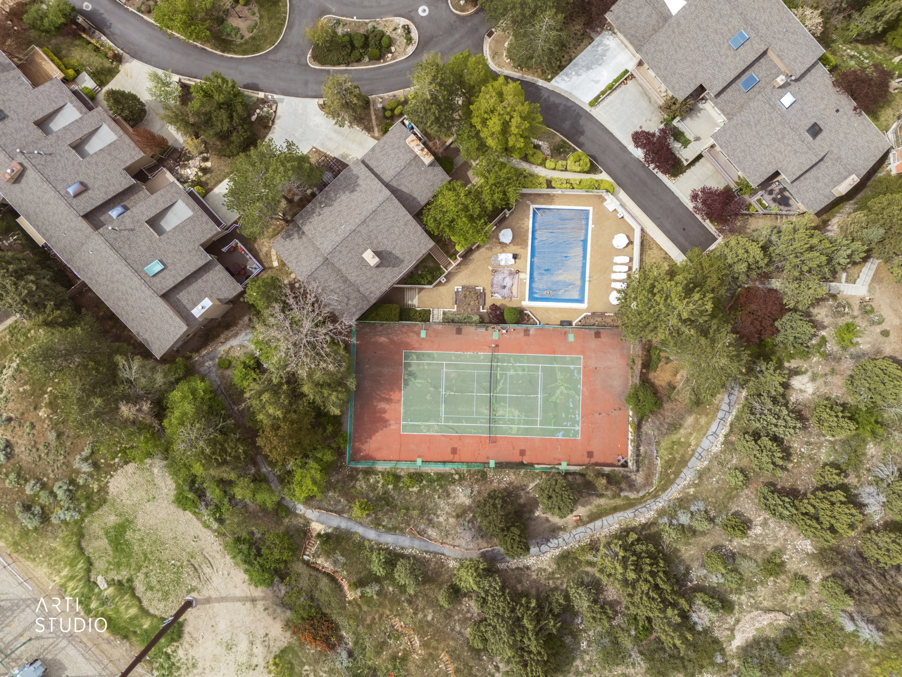Aerial view of HOA club and pool area featuring a private tennis court with a red and green surface, a rectangular swimming pool