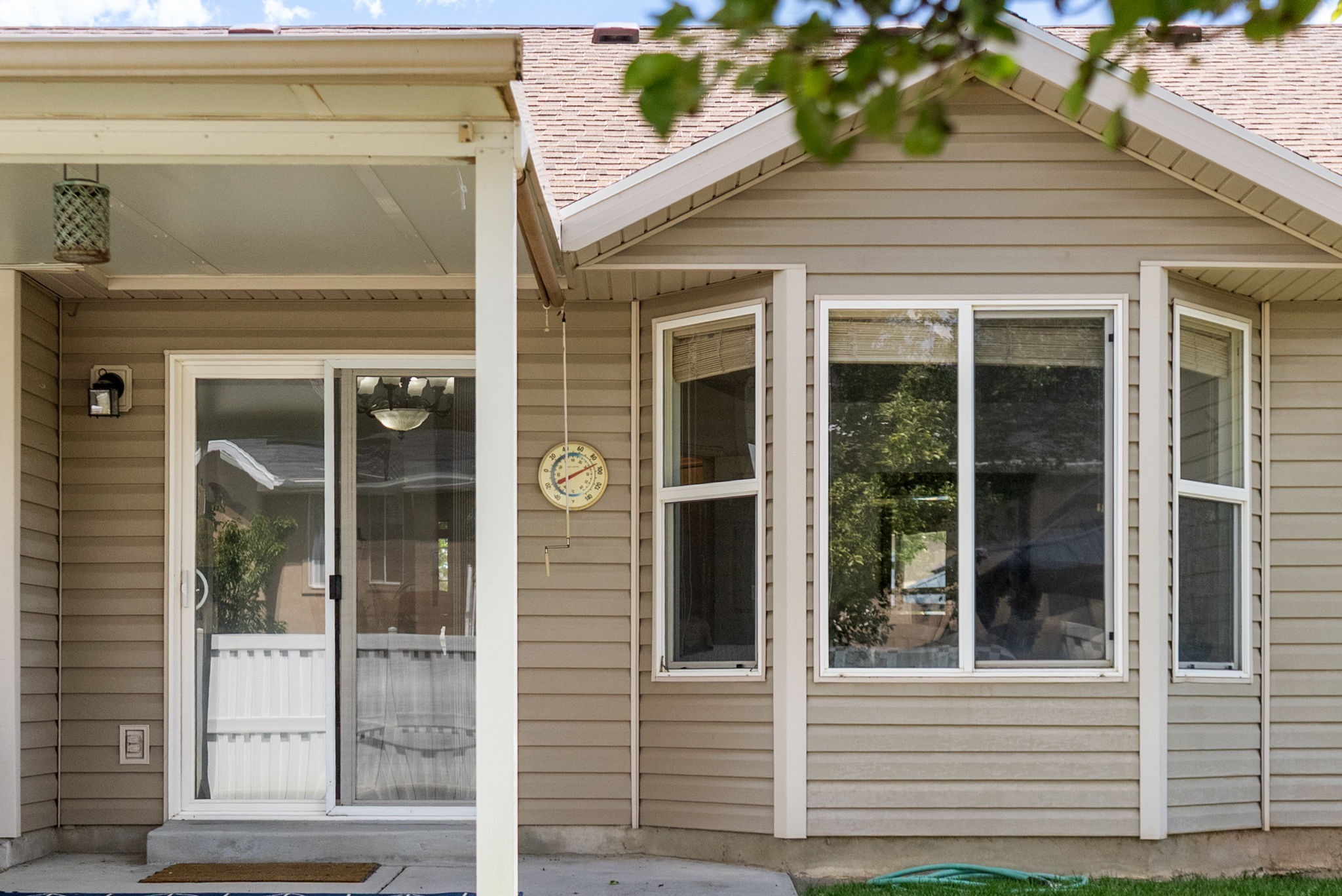 Exterior featuring beige horizontal siding, a covered patio area, a sliding glass door, and a multi-pane bay window