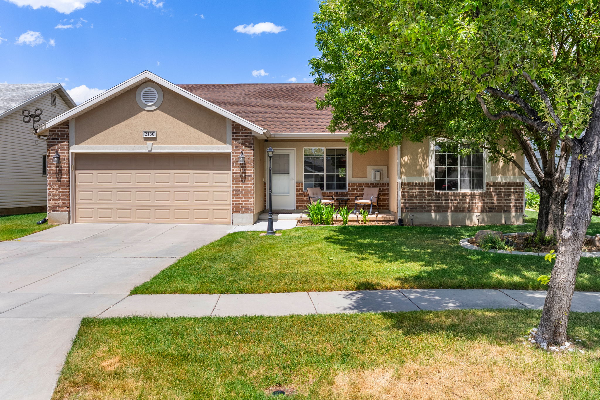 Single-story residence featuring a two-car garage, brick and stucco exterior, covered front porch, and mature landscaping