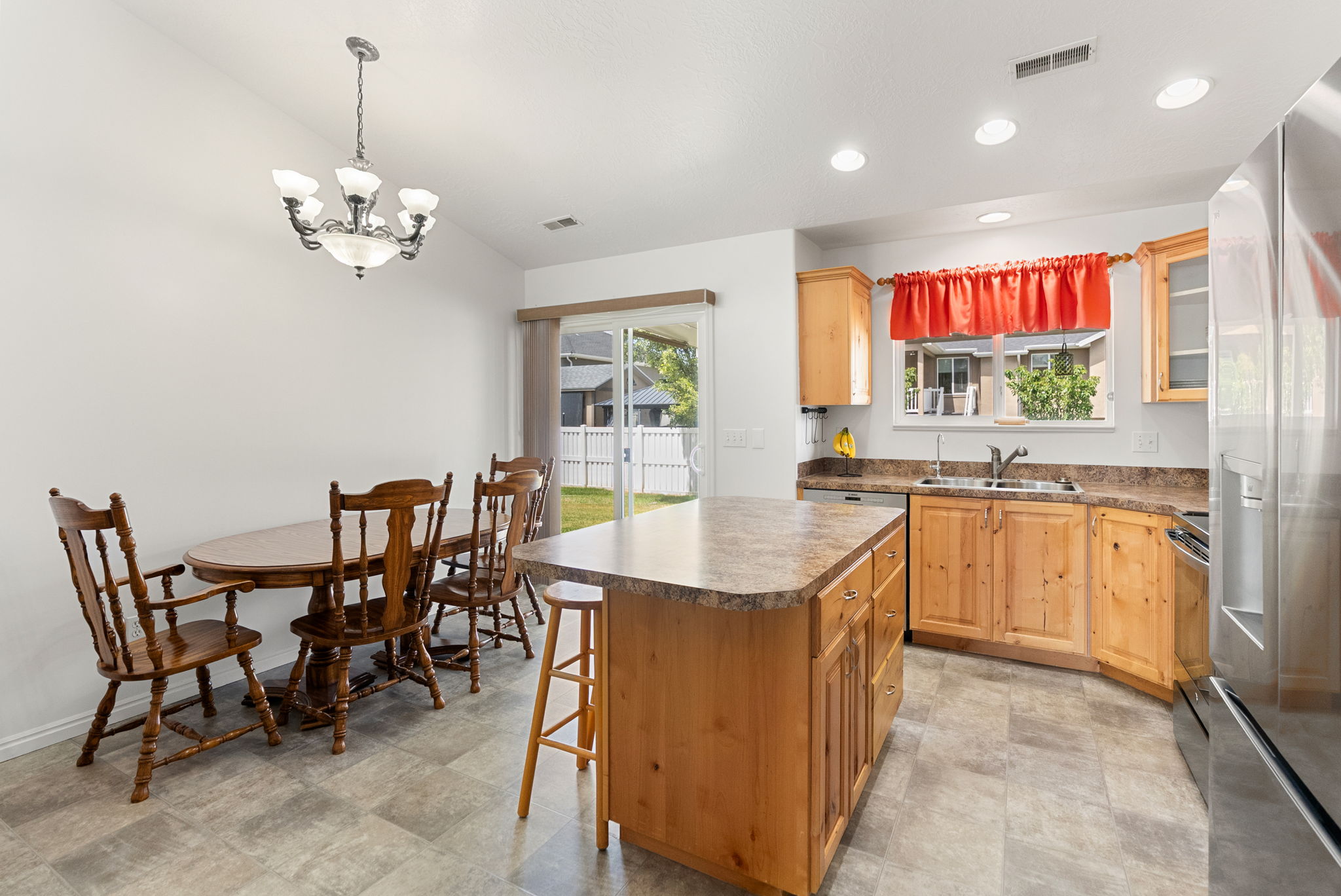 Open-concept kitchen and dining area featuring light wood cabinetry, a central island with an extended countertop, stainless steel appliances, and a sliding glass door providing exterior access