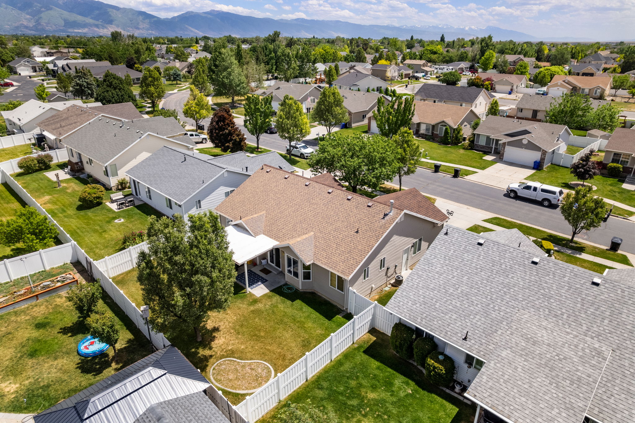 Aerial property view featuring a light-colored exterior, brown shingle roof, and a covered patio