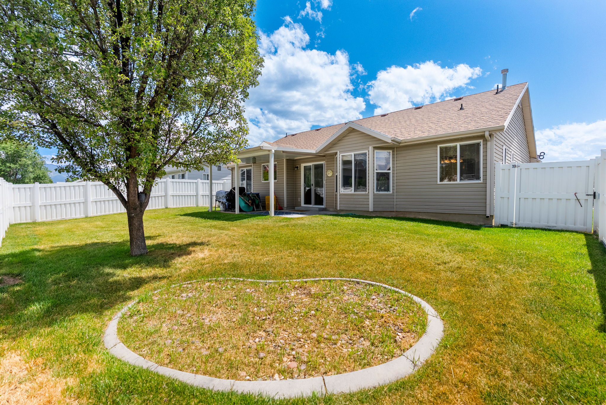 Expansive backyard featuring a mature tree, perimeter vinyl fencing, and a covered patio area