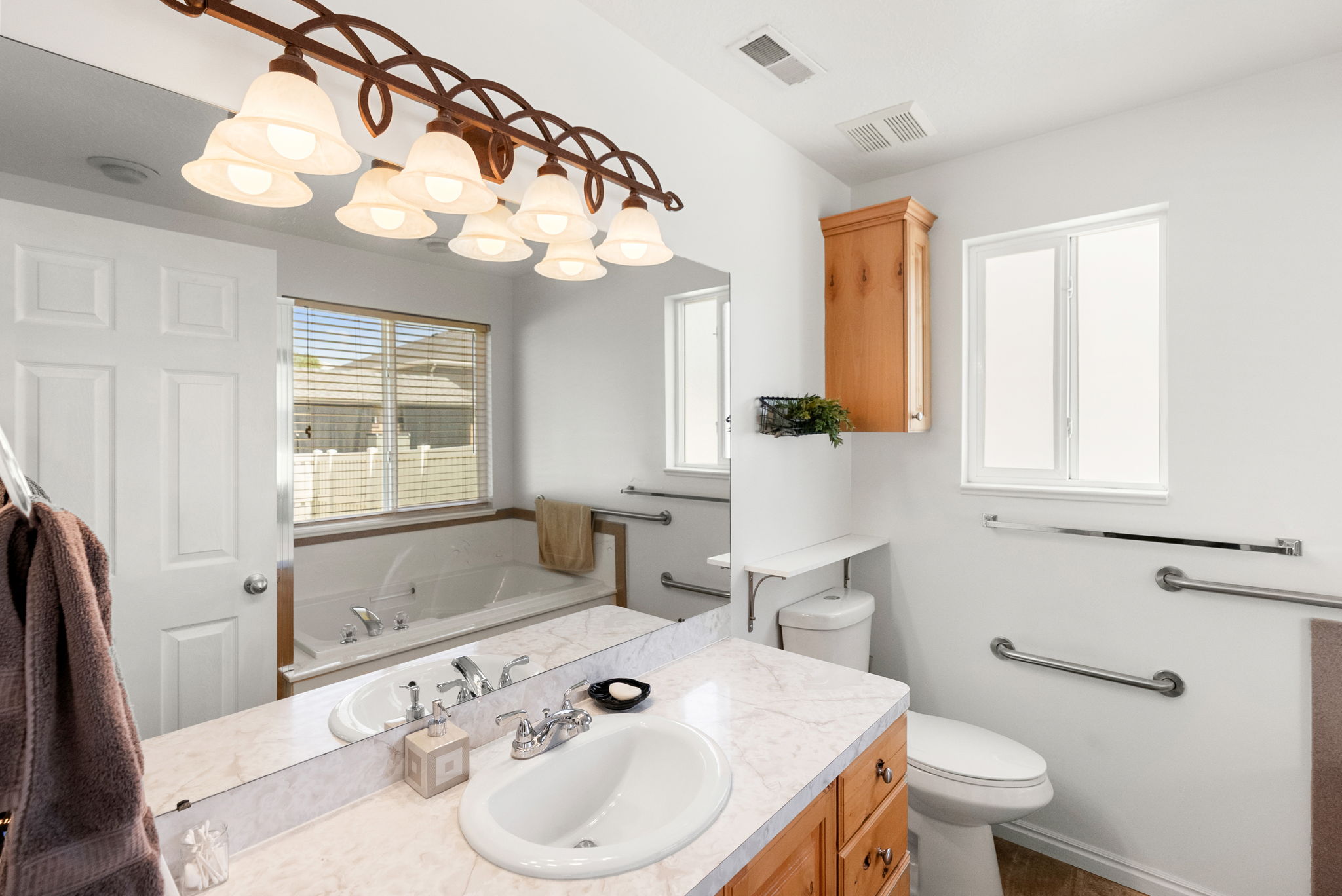Bathroom featuring a jetted tub, single vanity with a laminate countertop, natural wood cabinetry, and multiple grab bars