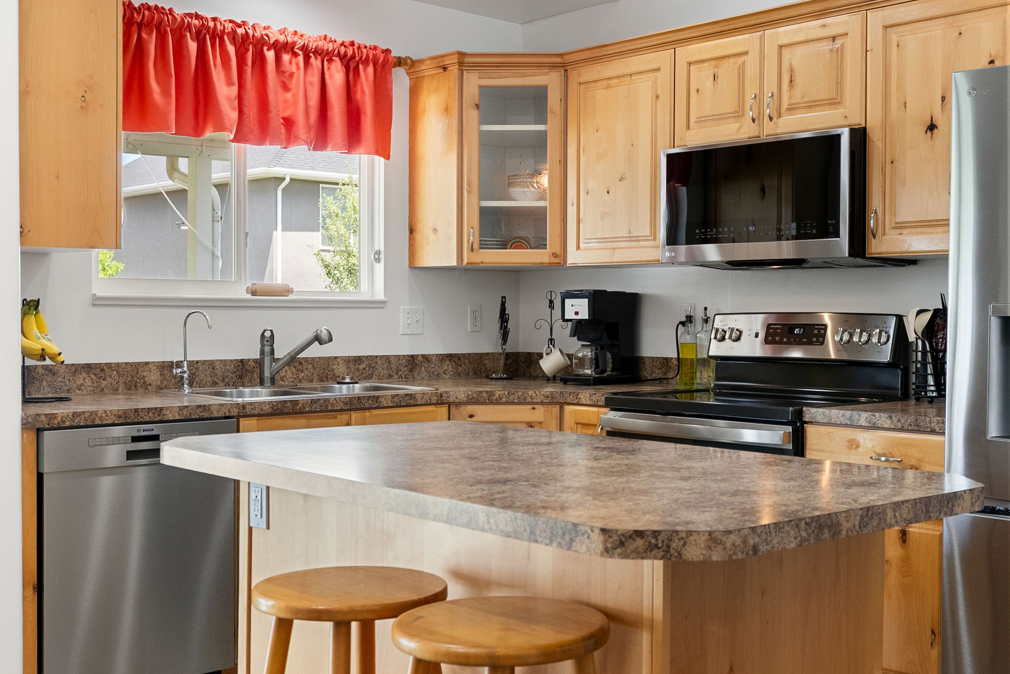 Kitchen featuring light wood cabinetry, stone-finish countertops, stainless steel appliances, and a central island with bar seating