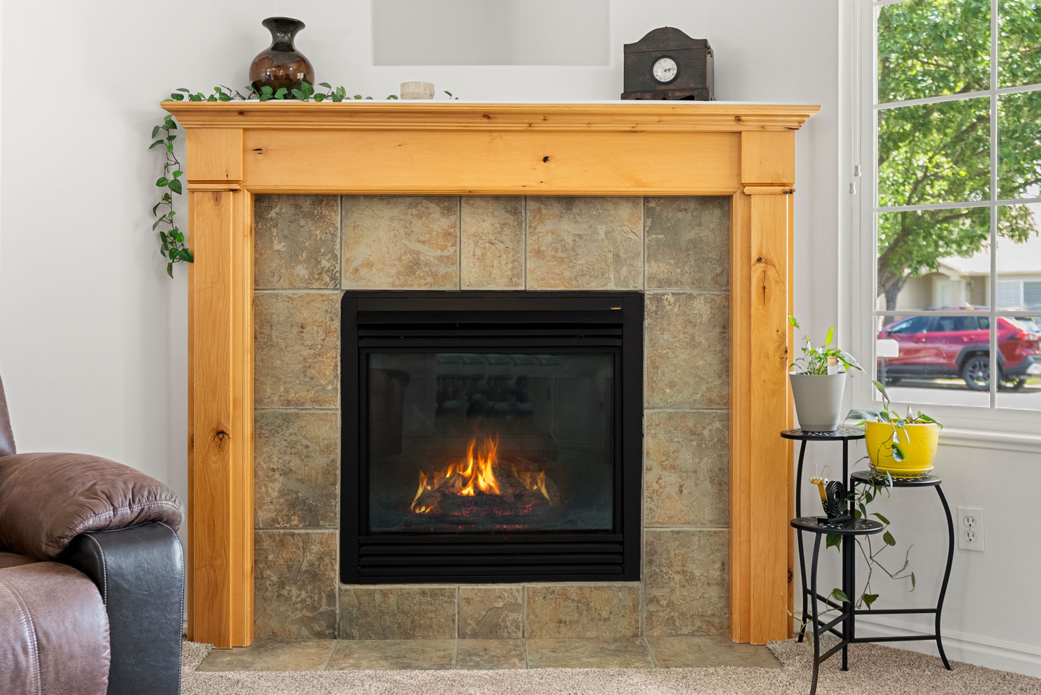 Fireplace featuring a light wood mantel, tile surround, and a black firebox with glass doors