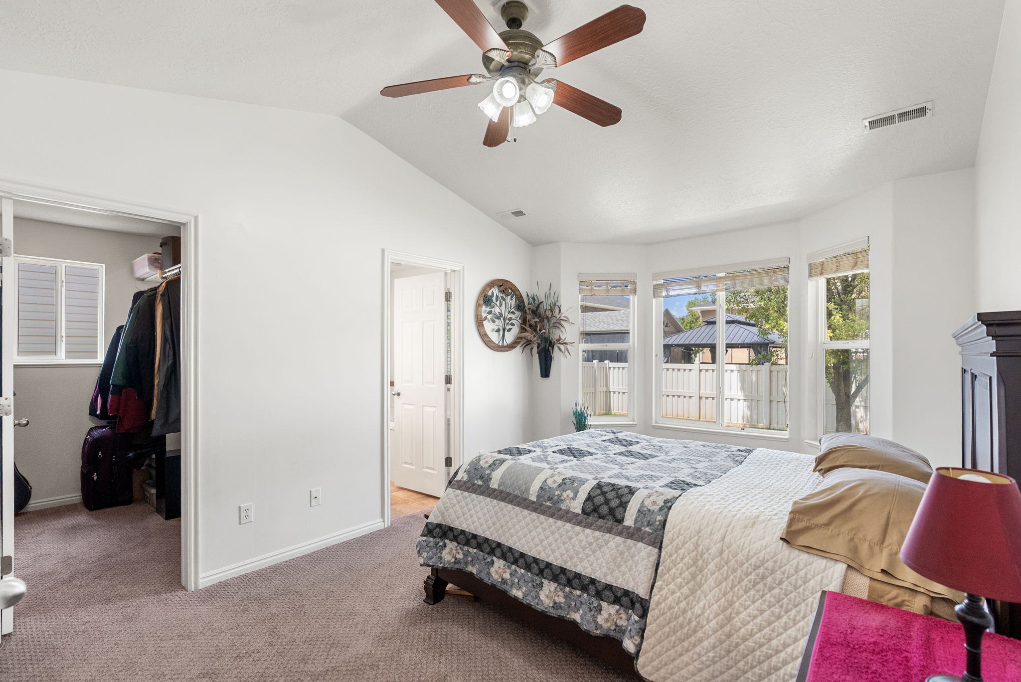 Vaulted ceiling bedroom featuring a bay window, ceiling fan with light fixture, carpeted flooring, and a walk-in closet with built-in shelving