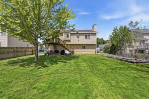 Expansive backyard featuring a manicured lawn, established shade tree, wood privacy fencing, a ground-level patio, and an upper-level wood deck with staircase access