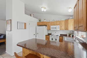 Kitchen featuring a spacious peninsula with a stone-finish countertop, wood cabinetry, and a white appliance suite