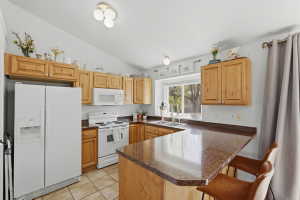 Kitchen featuring light wood cabinetry, white appliances, and a peninsula countertop