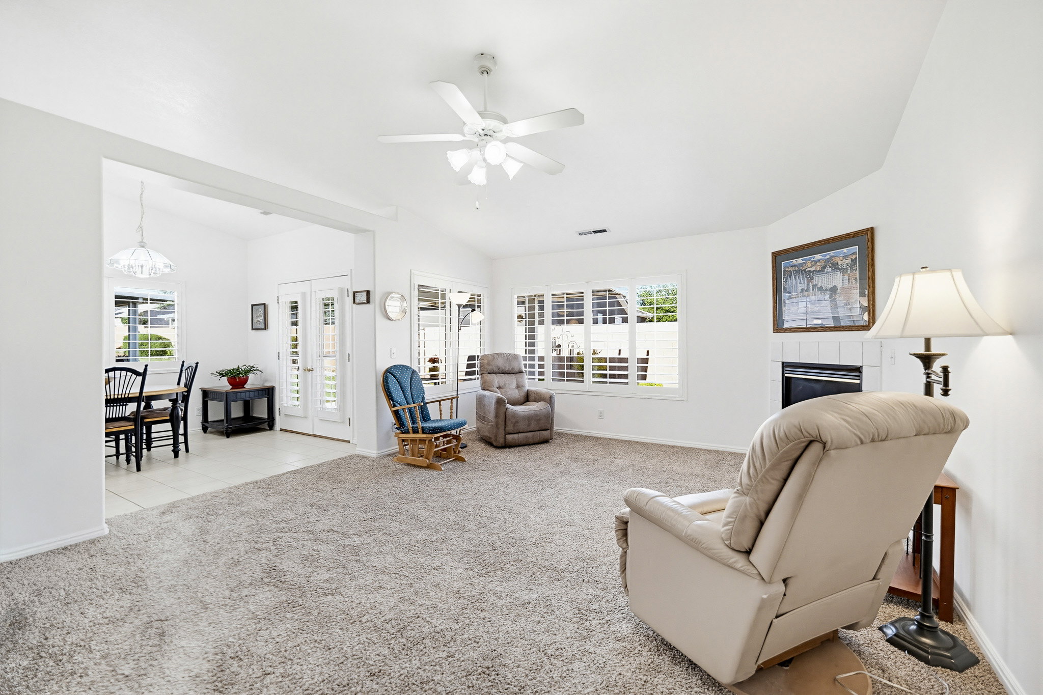 Spacious living area featuring carpet flooring, a ceiling fan, and a corner fireplace with a white tile surround