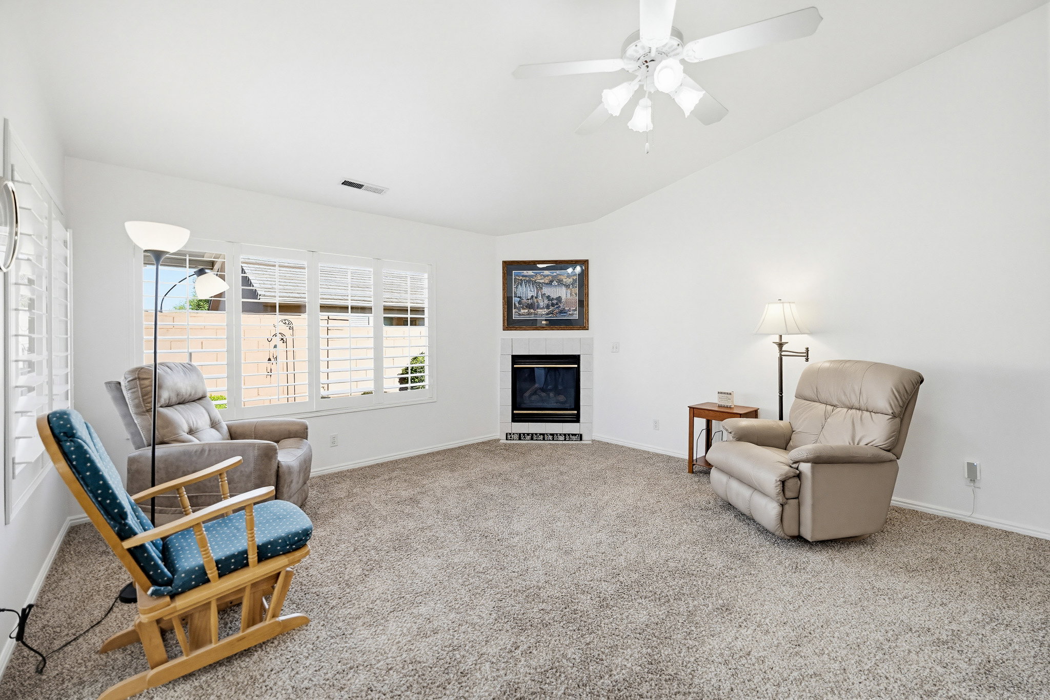 Carpeted living space featuring white walls and a corner fireplace with a dark mantel