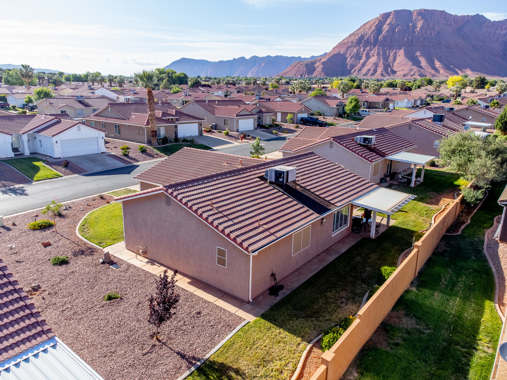 Terracotta-tiled roof property featuring a stucco exterior, an extended patio cover, a manicured lawn, and a perimeter fence