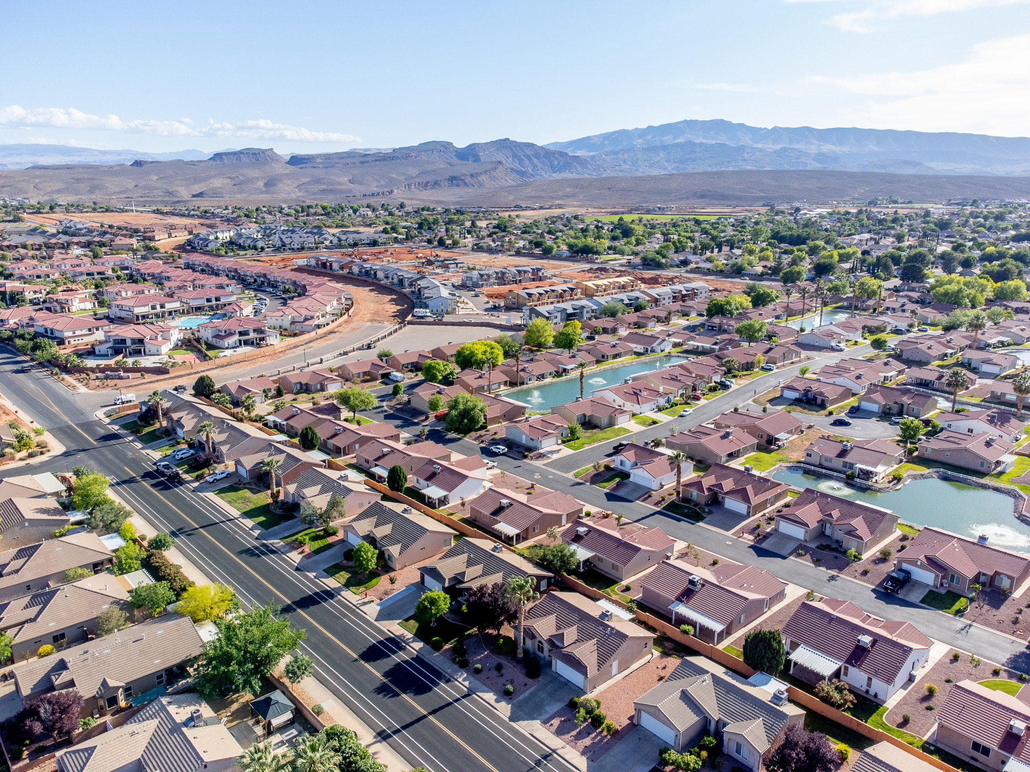 Aerial perspective showcasing a residential community with mature landscaping, multiple water features, and mountain scenery