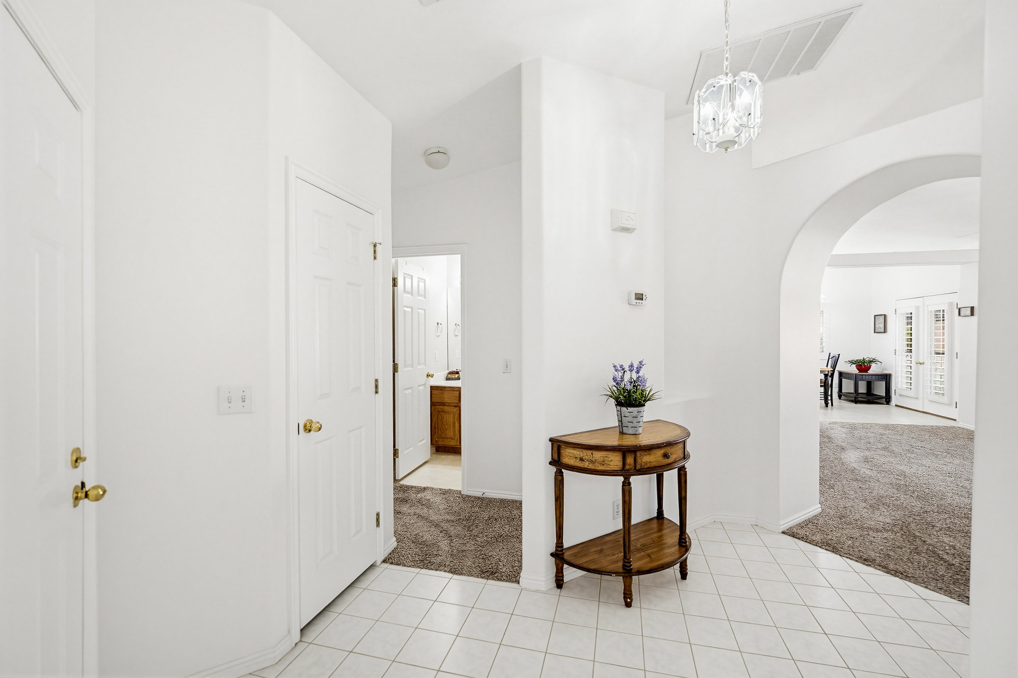Entryway featuring white tile flooring, white paneled doors with brass hardware, and a decorative archway opening to a carpeted room