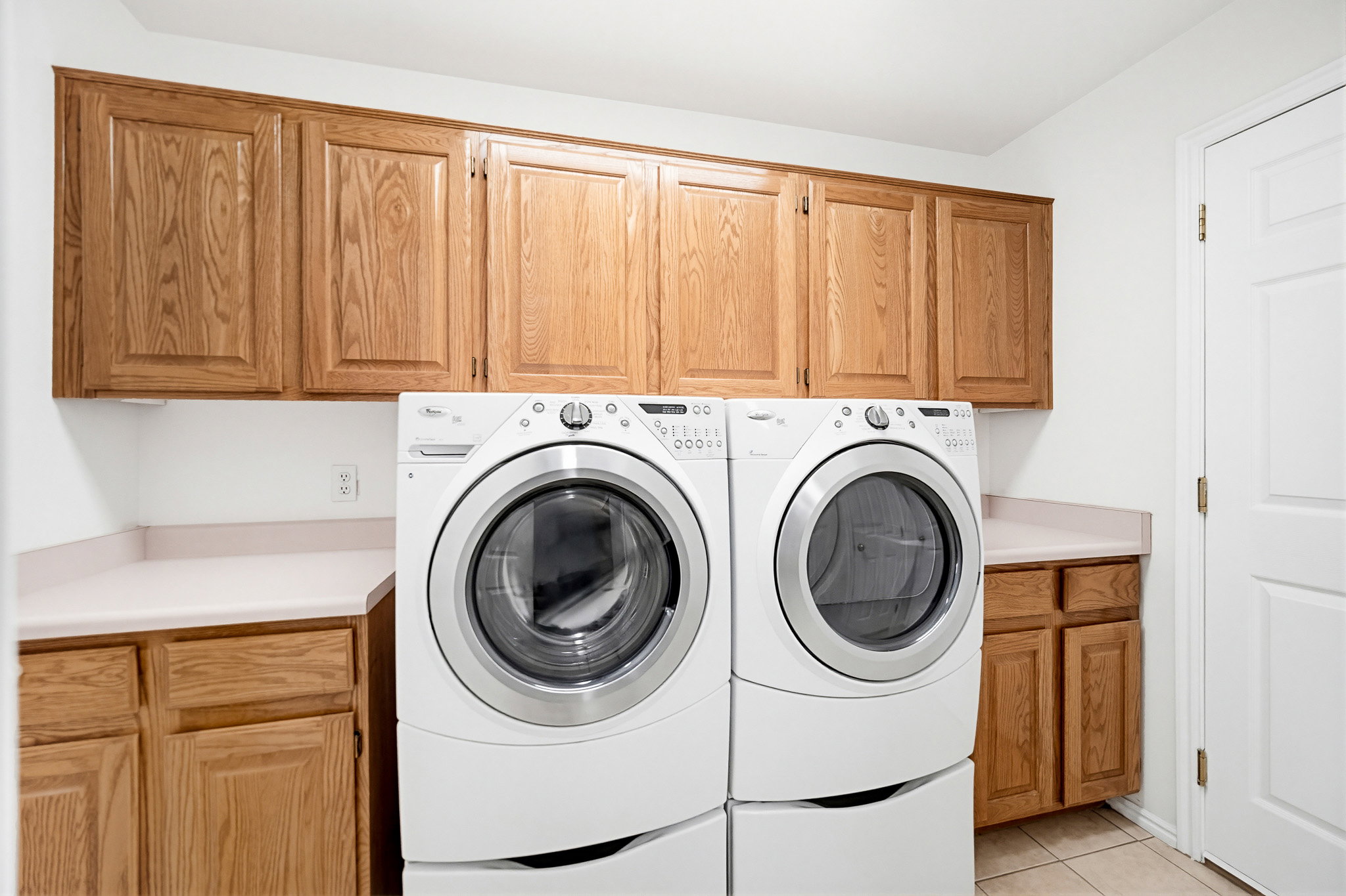 Dedicated laundry room featuring light wood-finish cabinetry, light countertops, and tile flooring