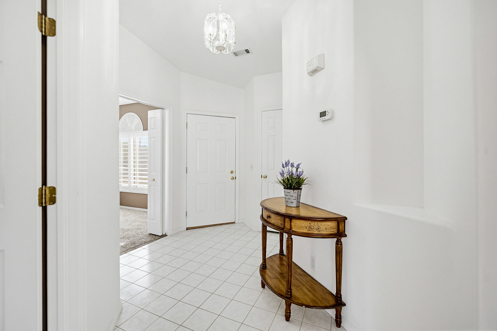 Bright entryway featuring white tile flooring, a paneled entry door, and a decorative ceiling light fixture