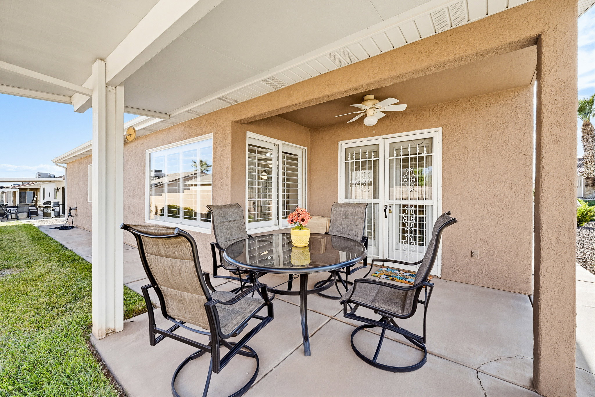 Covered patio with a concrete slab, stucco exterior, ceiling fan, sliding glass doors with security grates, and a lawn area