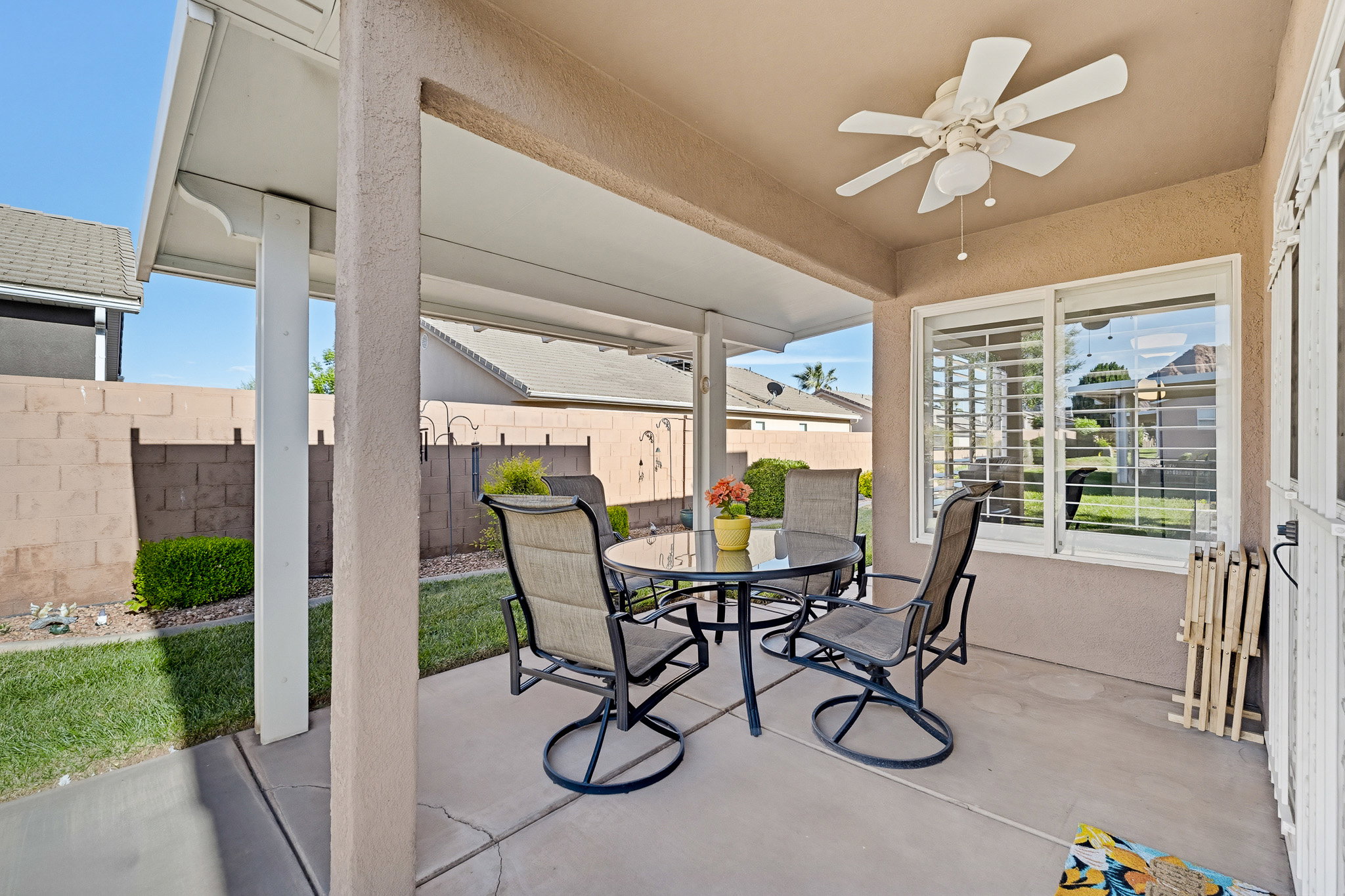 Covered patio space featuring a ceiling fan, sliding window with horizontal blinds, and a block wall perimeter