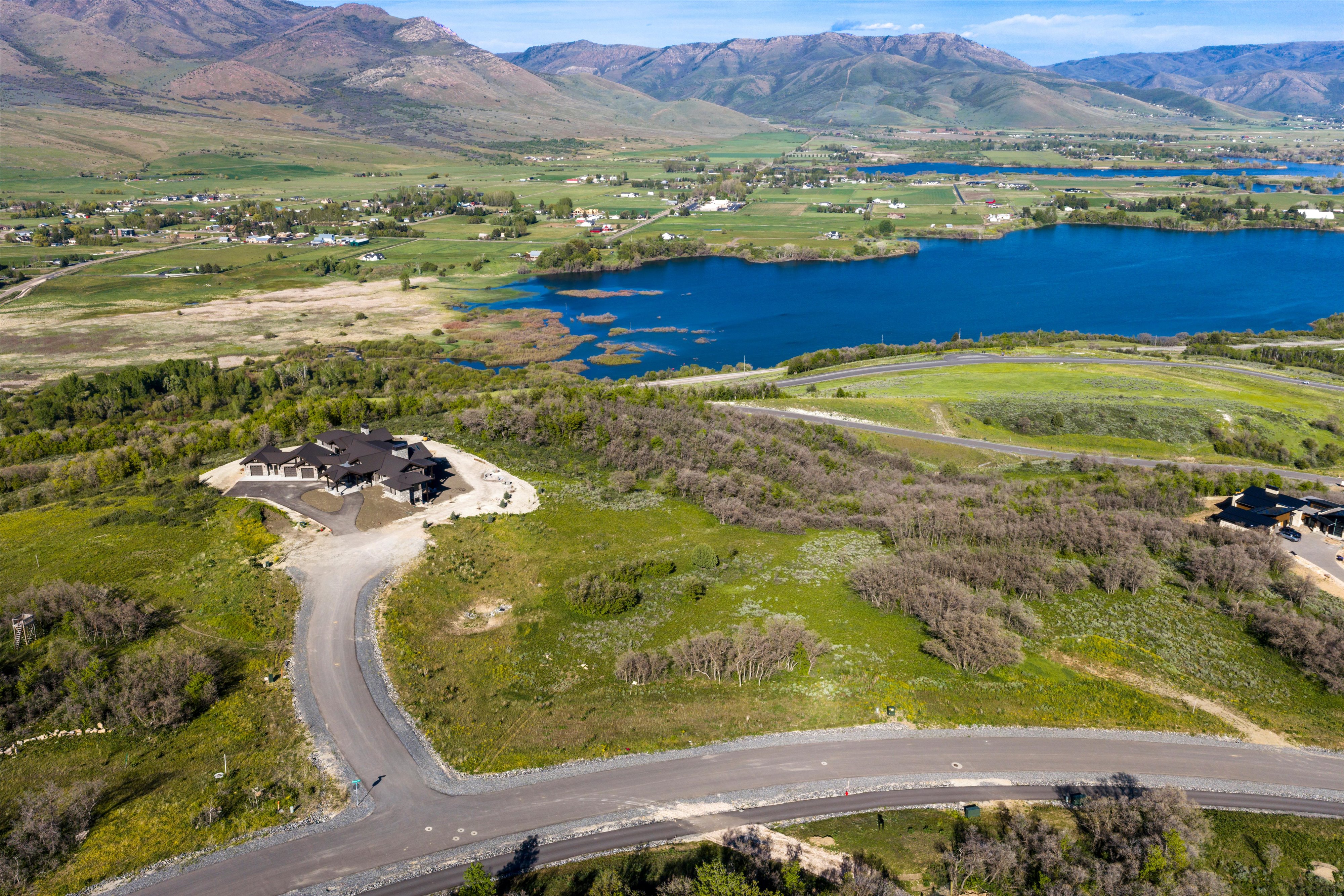Expansive property featuring a contemporary residence, a paved driveway, surrounding green landscapes, distant mountain ranges, and a visible body of water