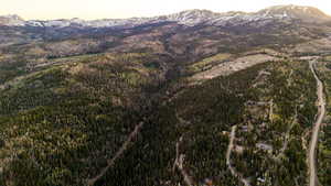 Expansive mountainous terrain featuring a dense forest, winding roads, and distant snow-capped peaks