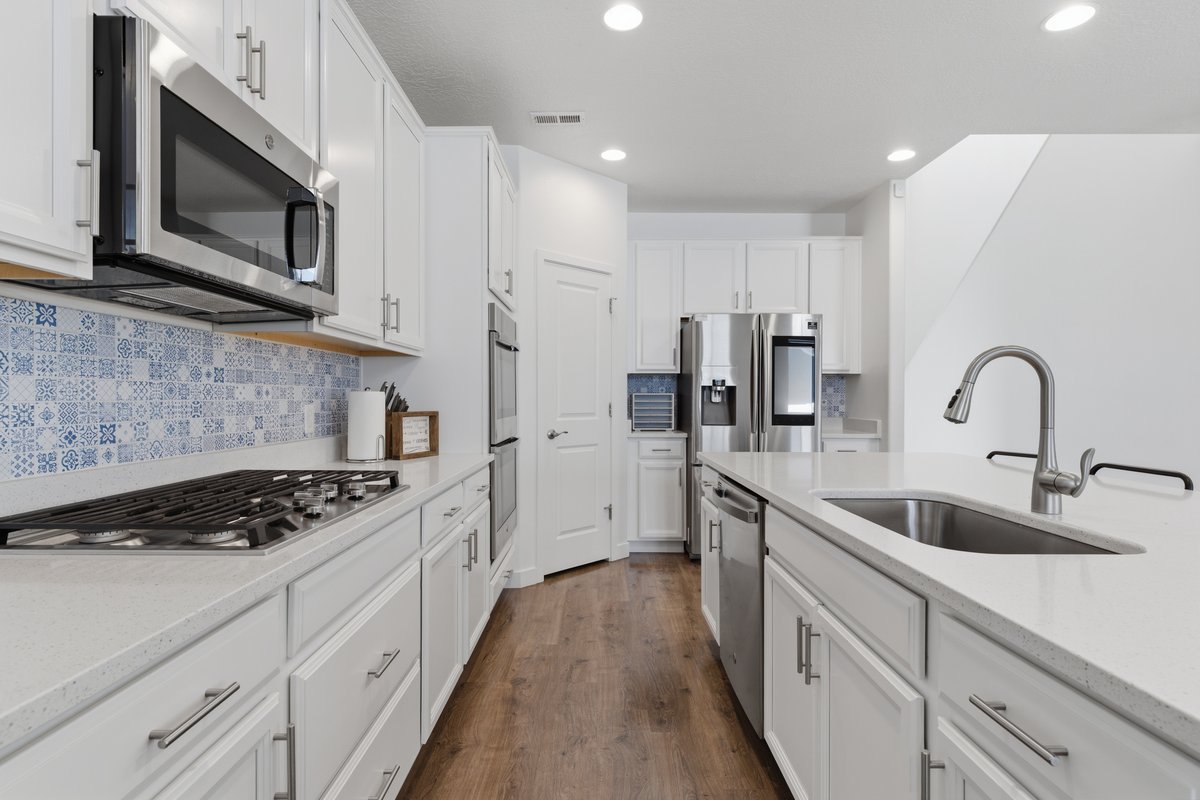 Contemporary kitchen featuring a gas cooktop, stainless steel appliances, white cabinetry with brushed nickel hardware, light-toned countertops, and wood-finish flooring