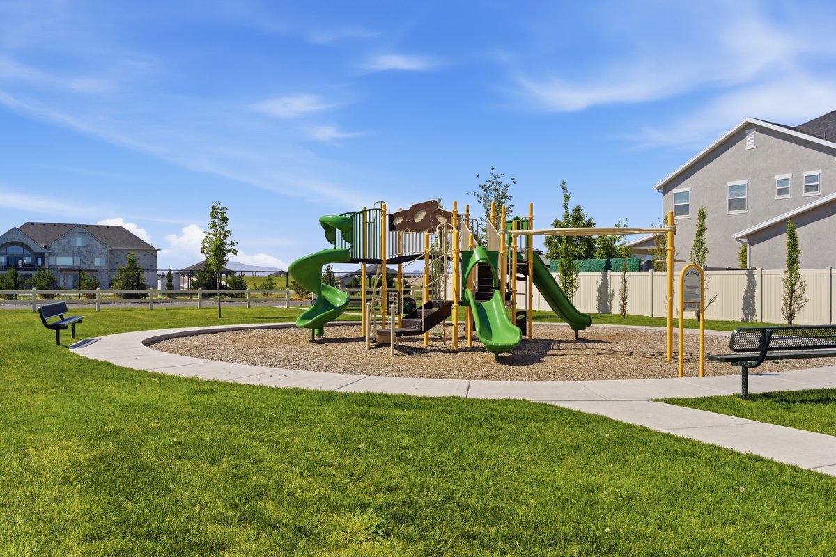 Community playground featuring multiple slides and climbing structures, surrounded by a paved walking path and grassy areas
