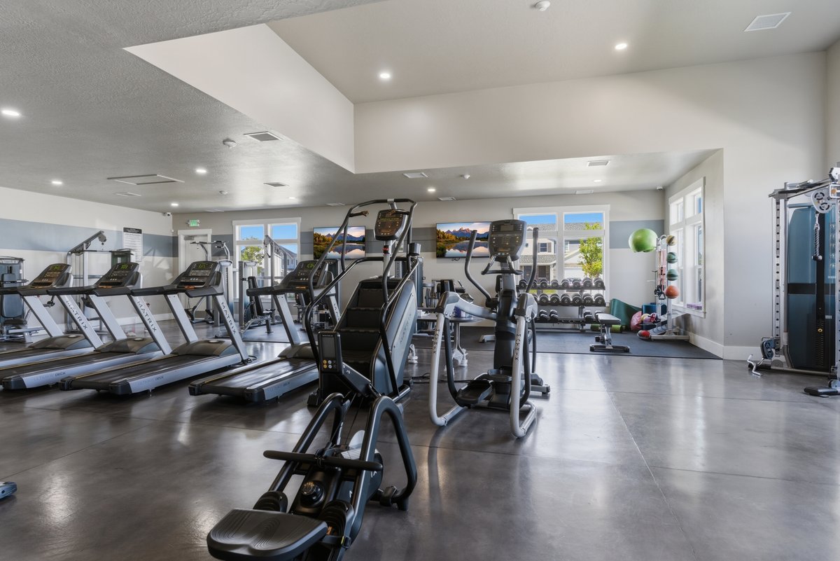 Community fitness center with multiple cardio machines, strength training equipment, large windows, recessed lighting, and polished concrete flooring