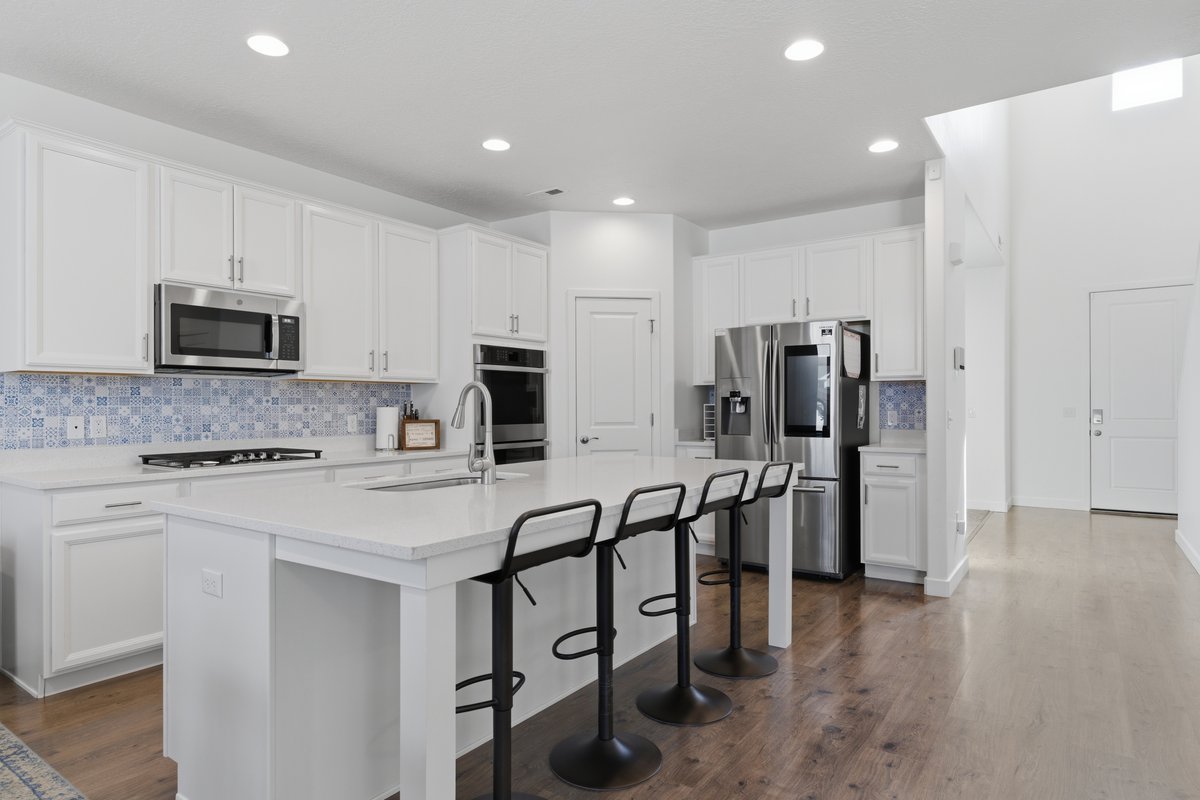 Contemporary kitchen featuring white cabinetry, a large center island with seating, stainless steel appliances, a mosaic tile backsplash, and recessed lighting