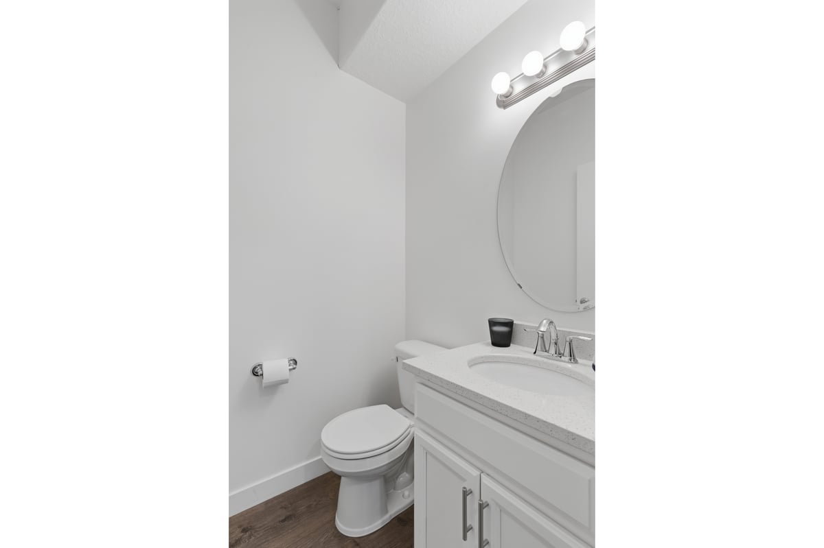 Powder room featuring a single vanity with an integrated sink, a round mirror, and a three-bulb vanity light fixture