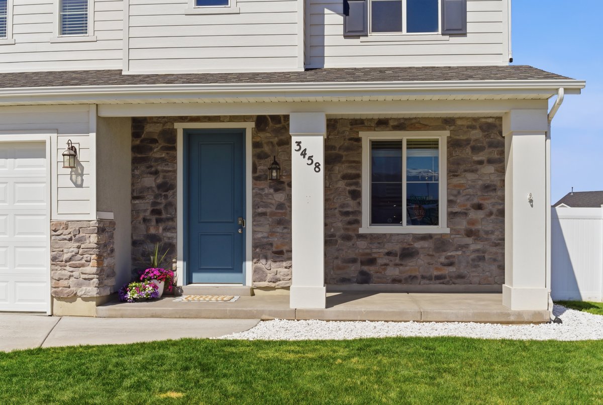 Covered entry featuring a blue paneled door, stone facade, white siding, and a concrete porch