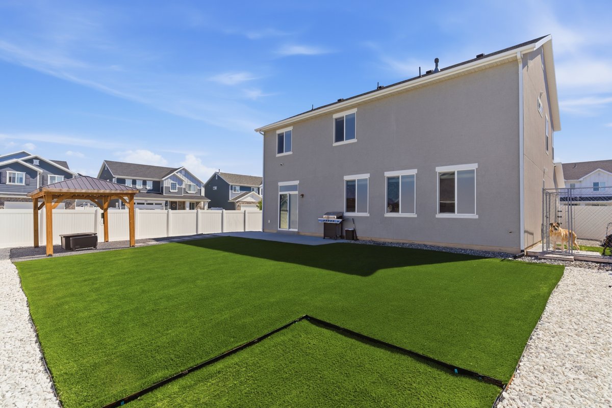 Spacious backyard featuring artificial turf, a white privacy fence, and a concrete patio