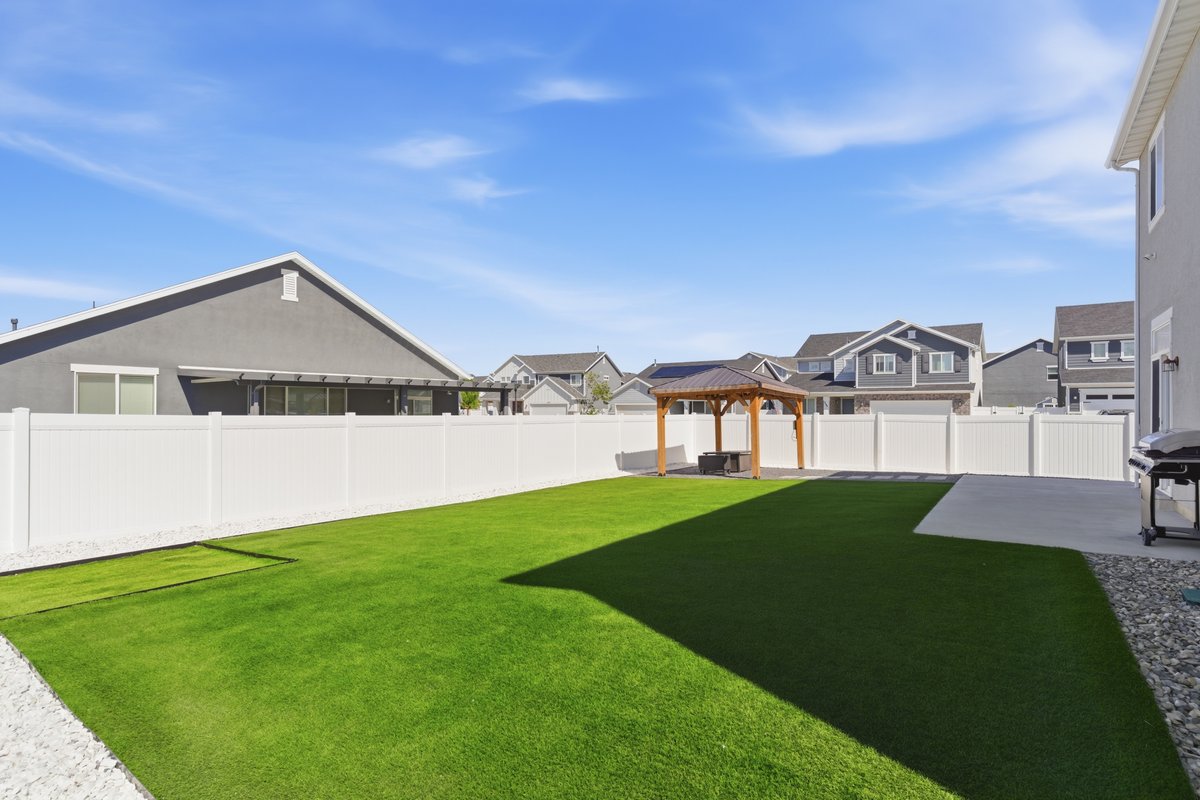 Expansive backyard featuring a lush green lawn, white privacy fencing, and a dedicated concrete patio area